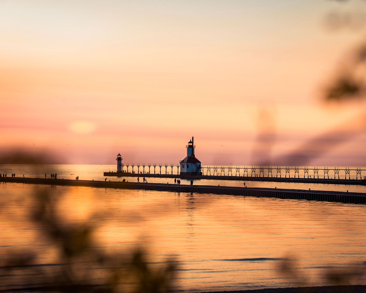 Misty waterfront view of pier and lighthouse during peaceful sunset.