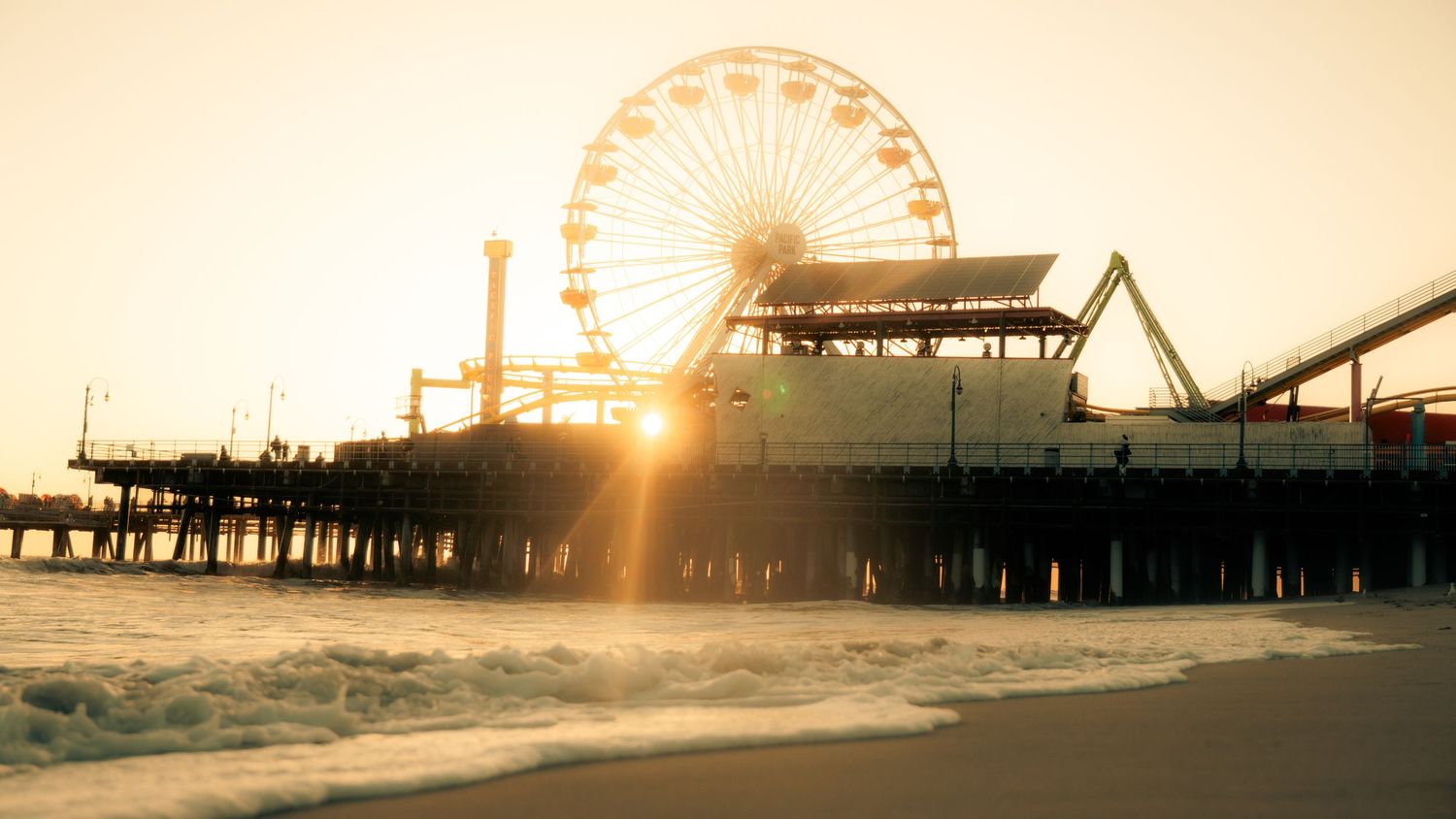 Panoramic silhouette of amusement park rides on pier during golden hour.