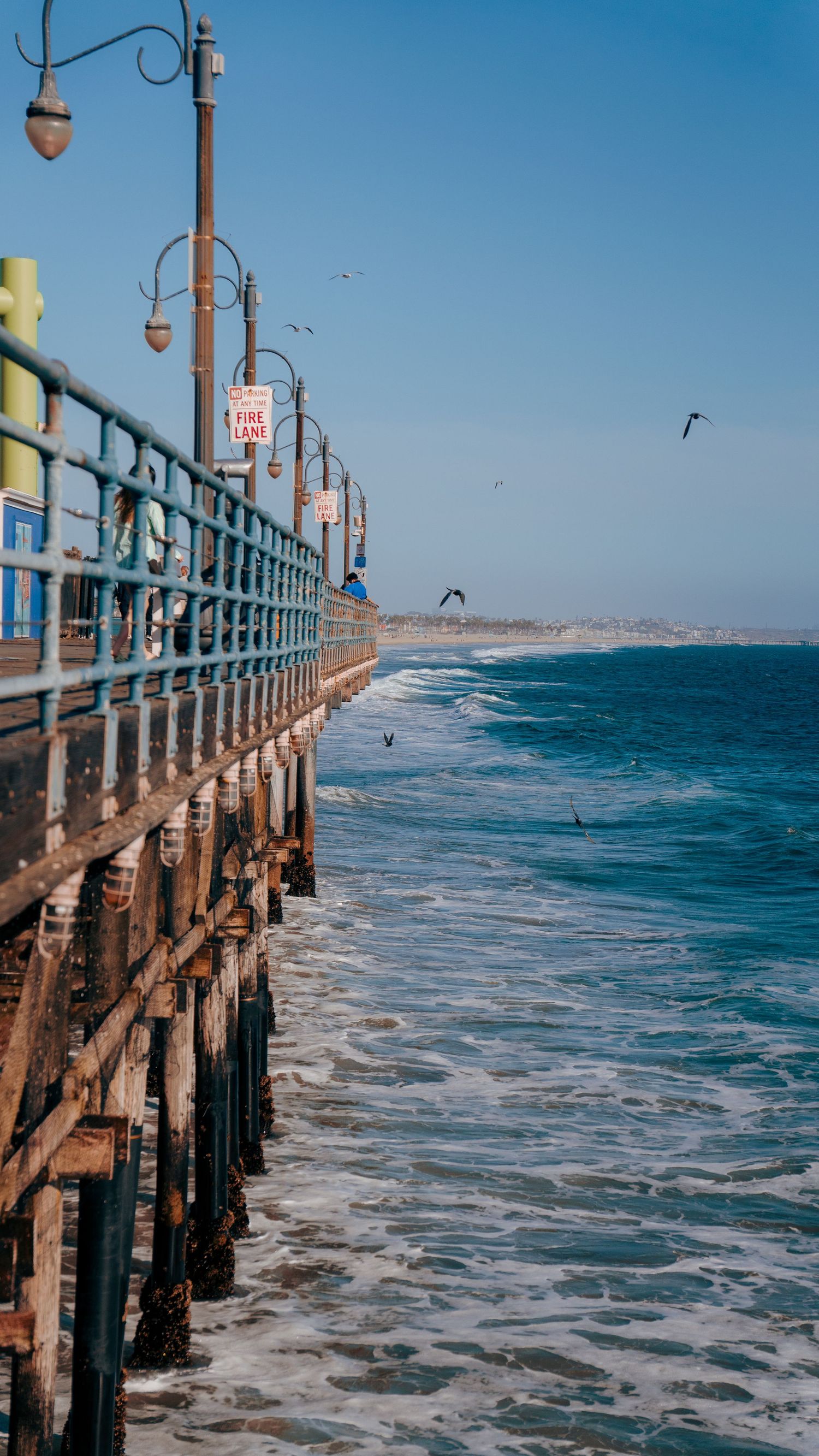 Historic wooden pier extends into blue ocean waters with waves crashing against the pillars.