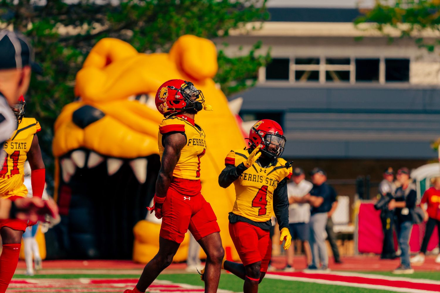 Football player in red and yellow uniform leaps high to catch the ball during a game on the field.