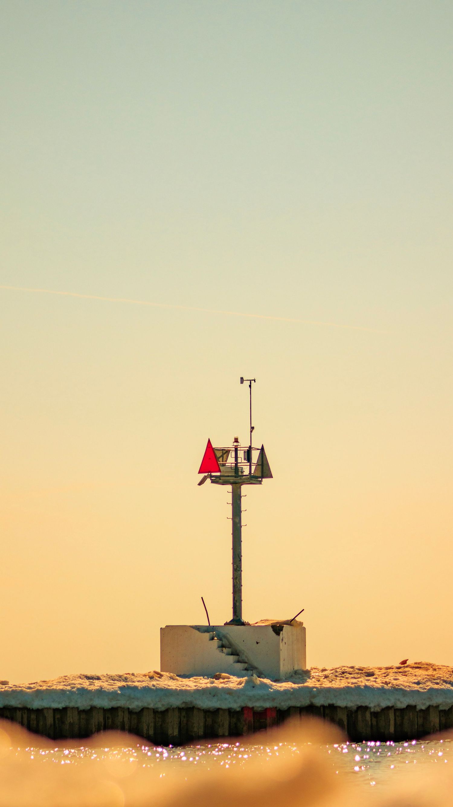 Channel marker with red triangle on pole standing above icy waters in sunset light.
