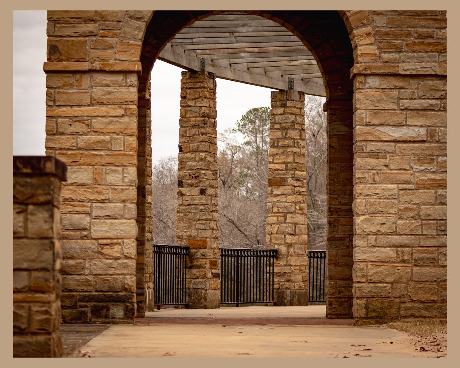 Stone archway entrance with pillars and iron gates in sepia tones.