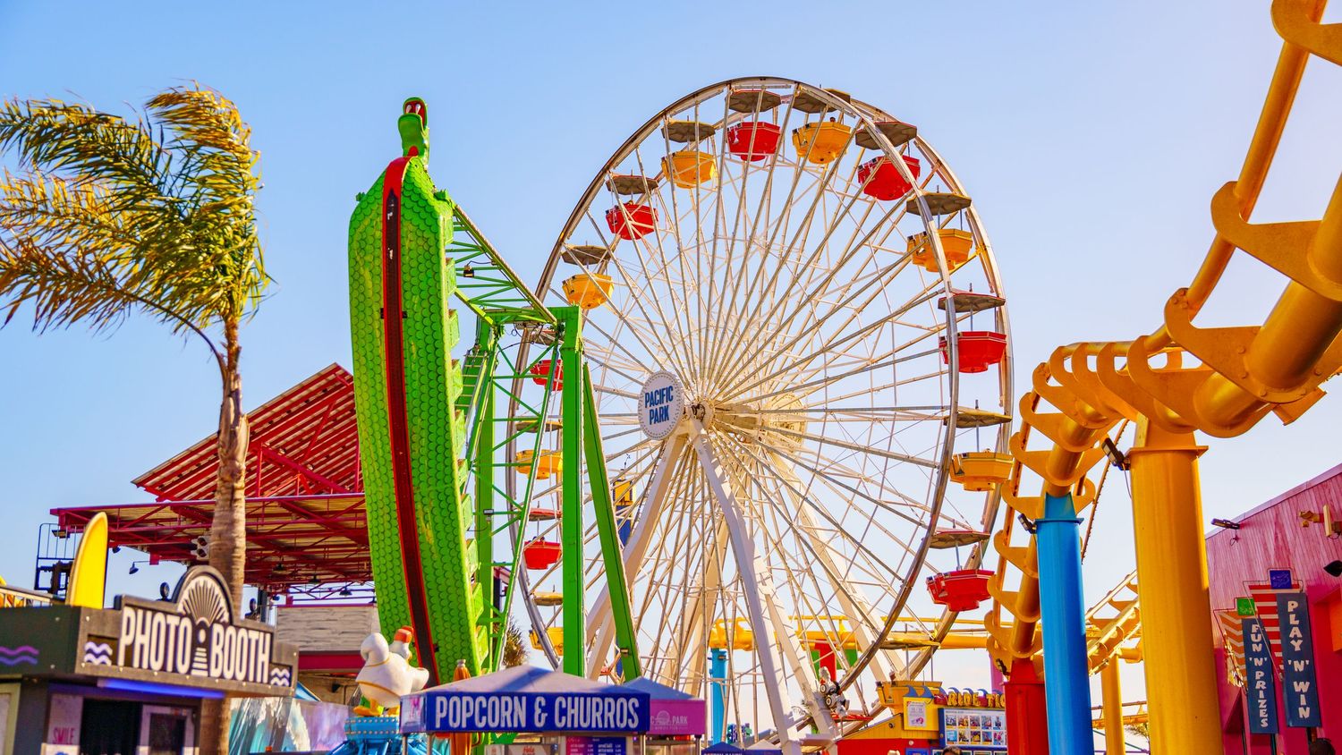 Vibrant carnival rides and Ferris wheel illuminate a bustling boardwalk with popcorn stands at sunset.