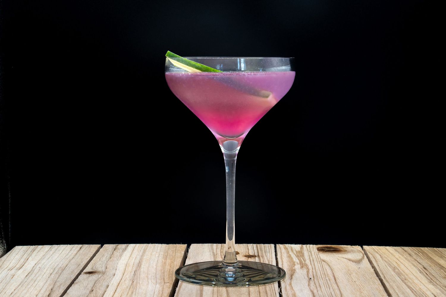 Pink cocktails in martini and coupe glasses on wooden surface against dark background.