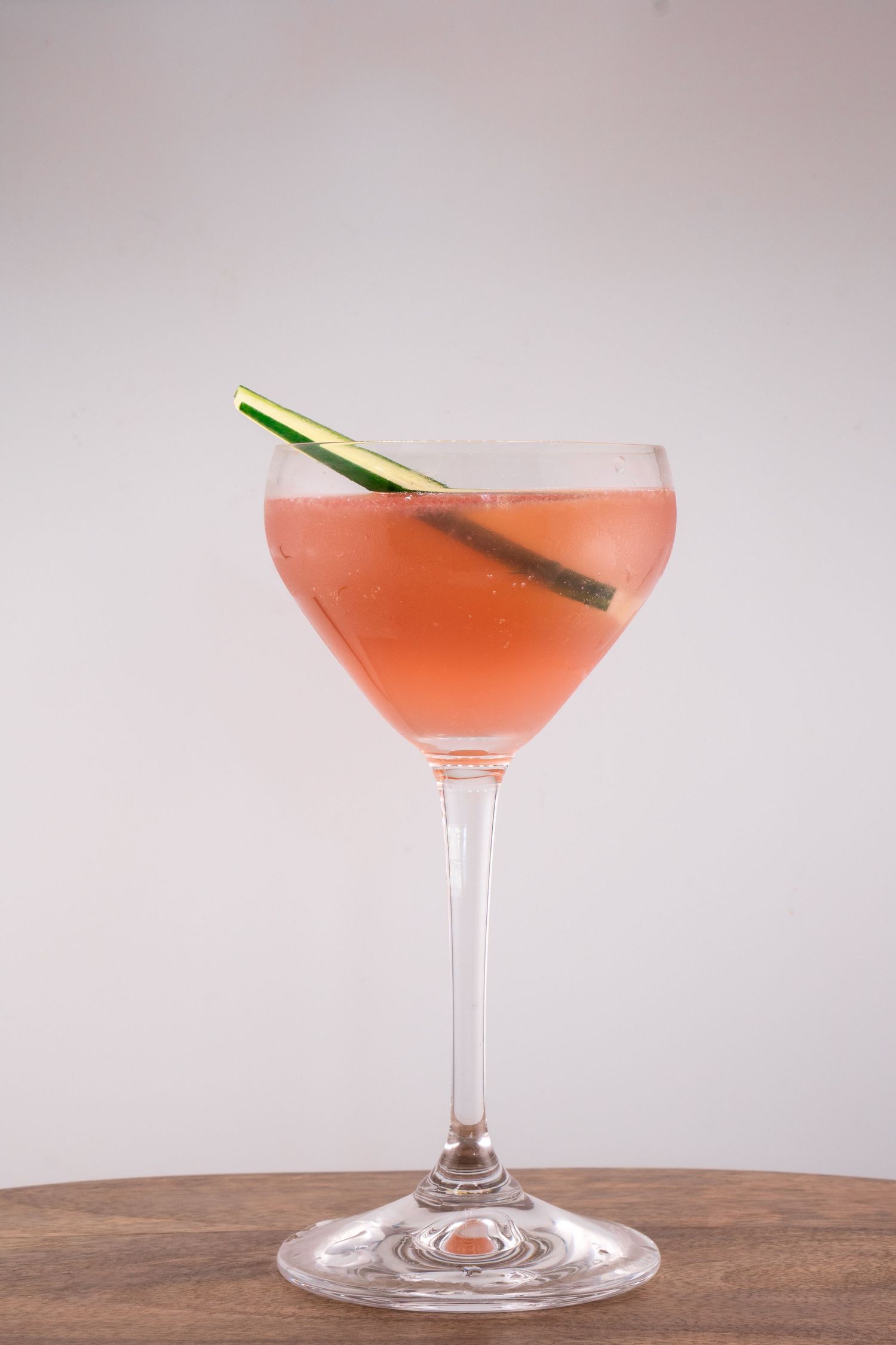 Pink martini cocktail with lemongrass garnish photographed on wooden surface.