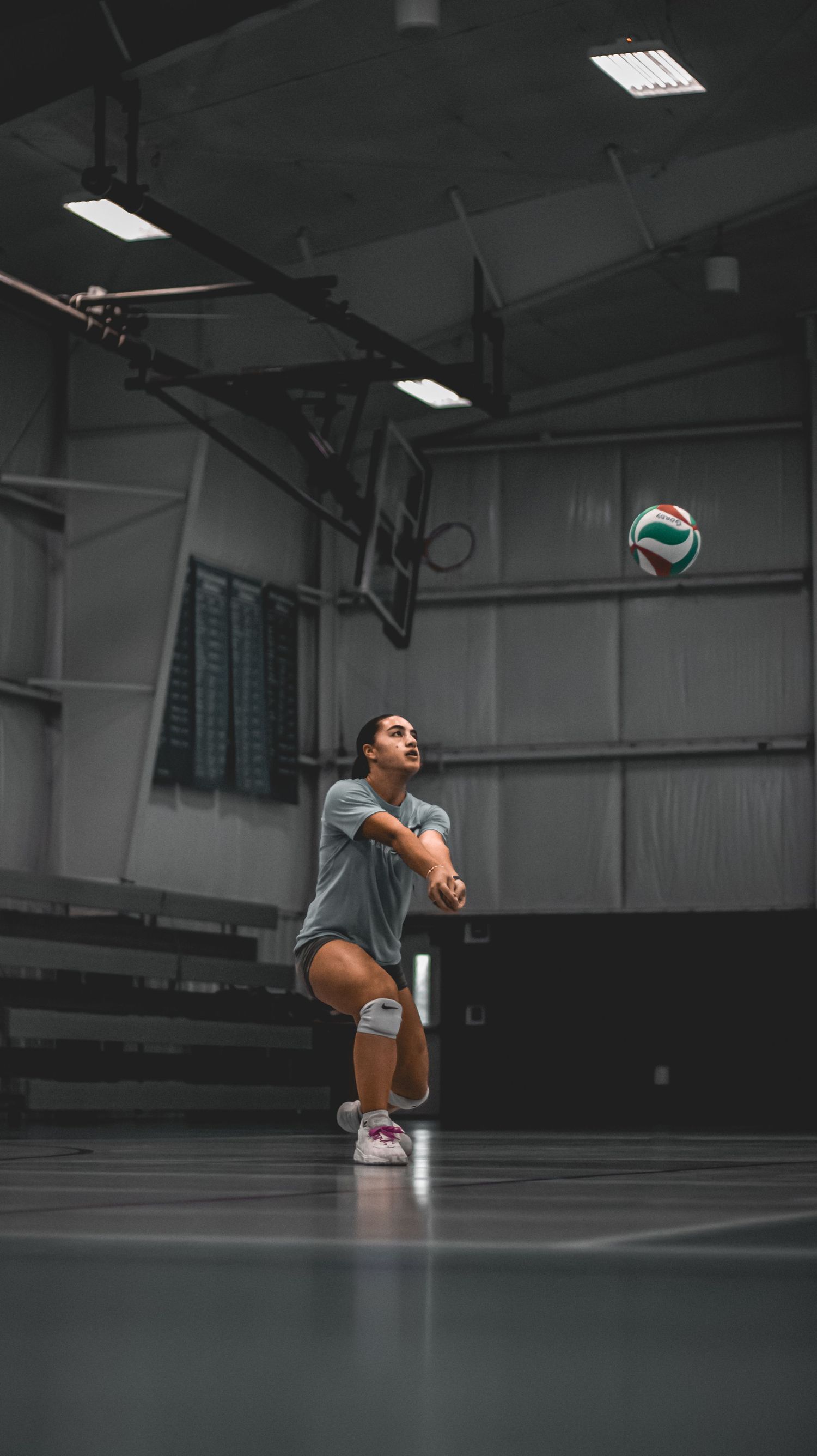 Player prepares to serve volleyball in dimly lit indoor court setting.