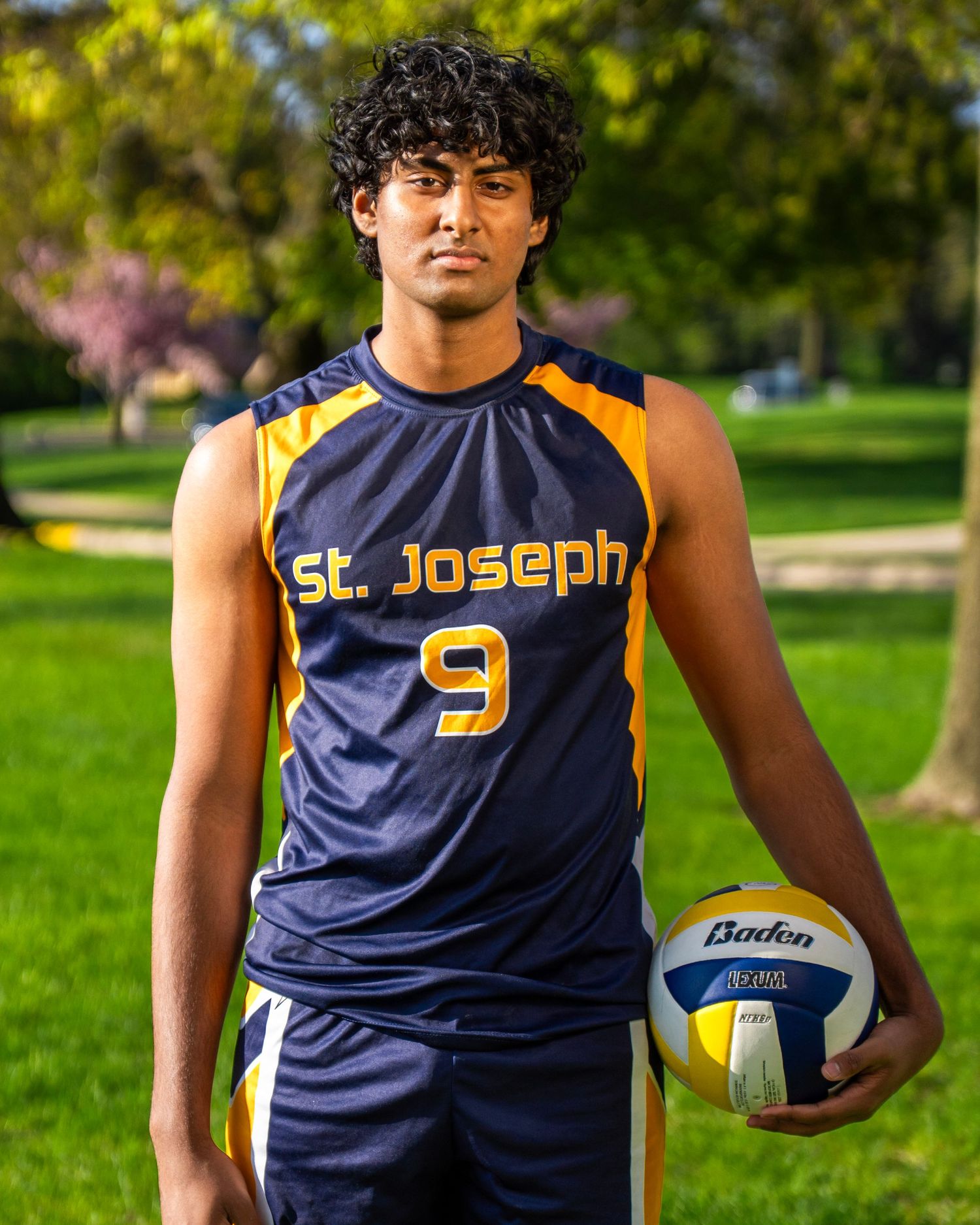 Athlete in St. Joseph navy jersey number 9 holds volleyball while standing on grass.