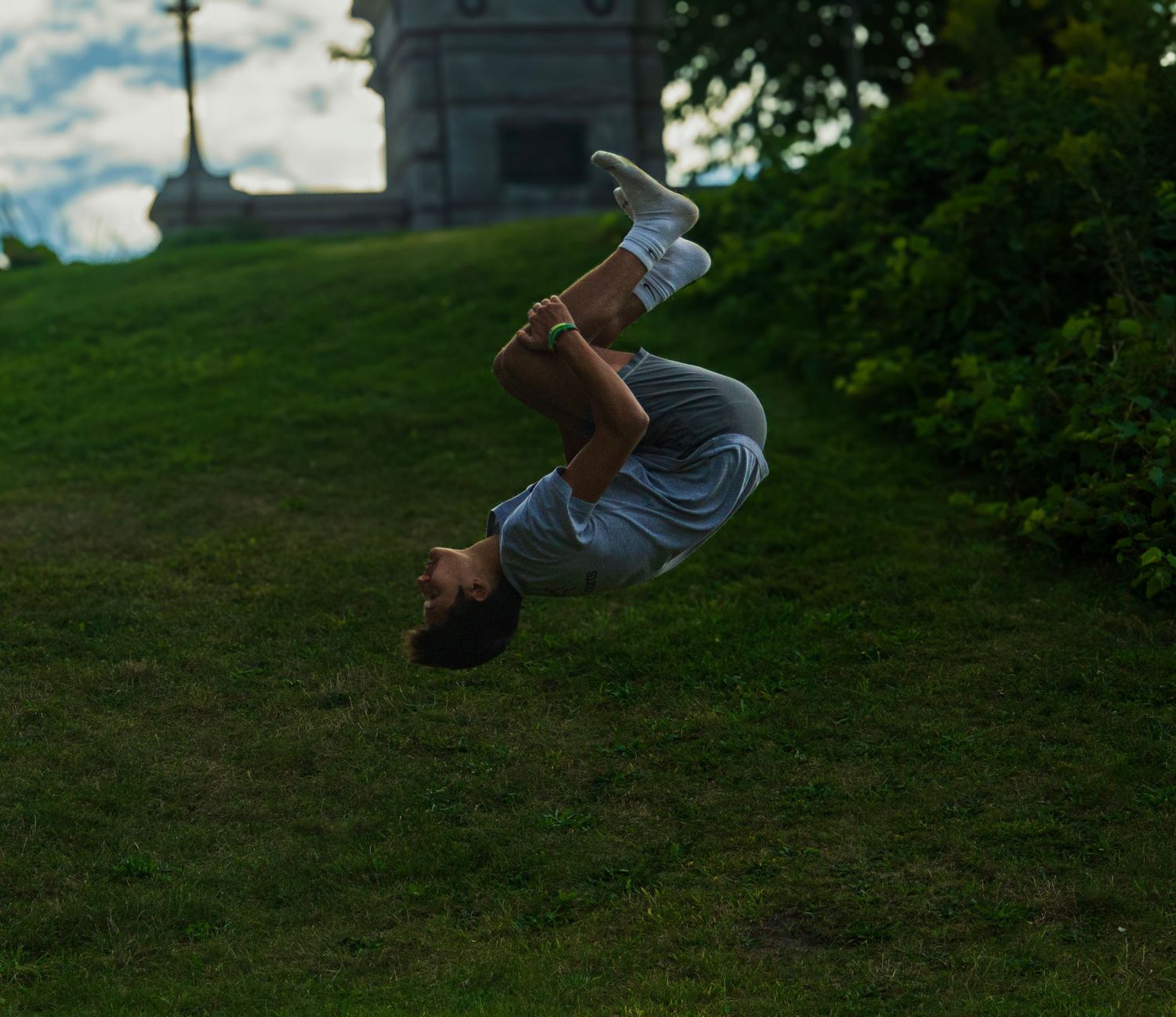 Person performing a backflip on a grassy hill with a tower in the background.