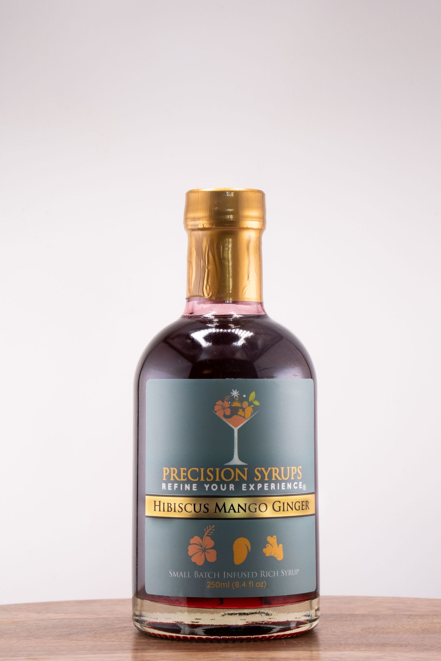 Bottle of Precision Syrups Hibiscus Mango Ginger with gold cap on wooden surface.
