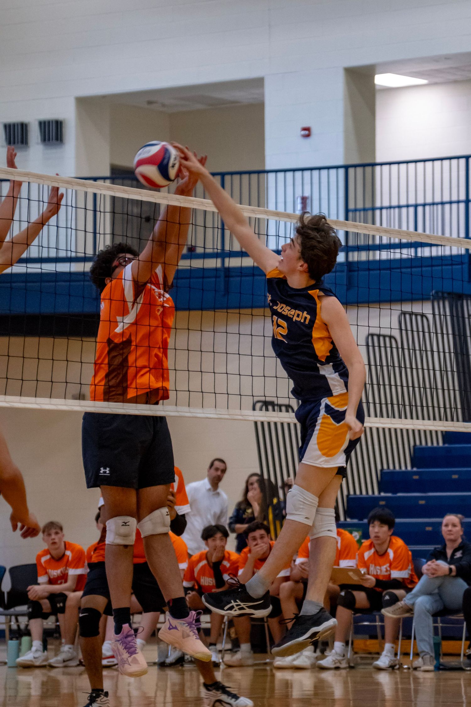 Athletes jump at the net during an intense volleyball rally in a school gymnasium.
