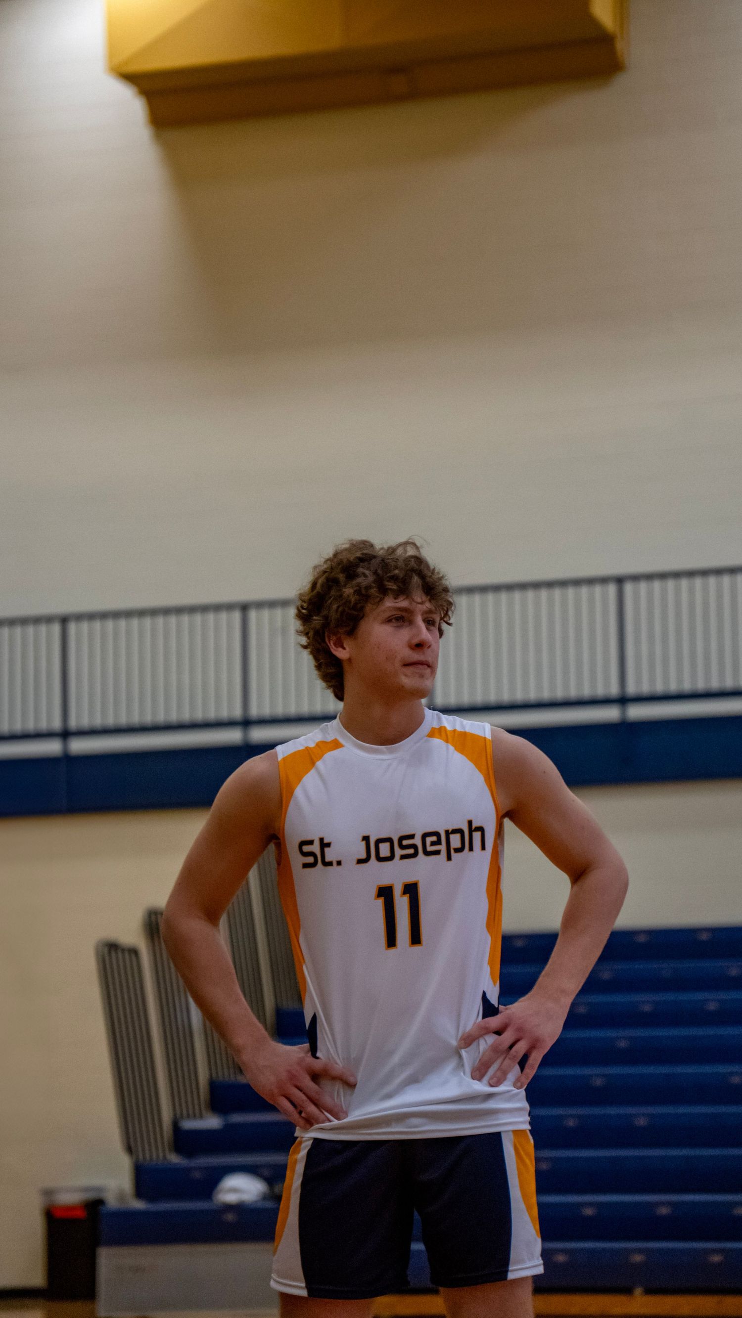 A player in a white St. Joseph uniform stands on the volleyball court.
