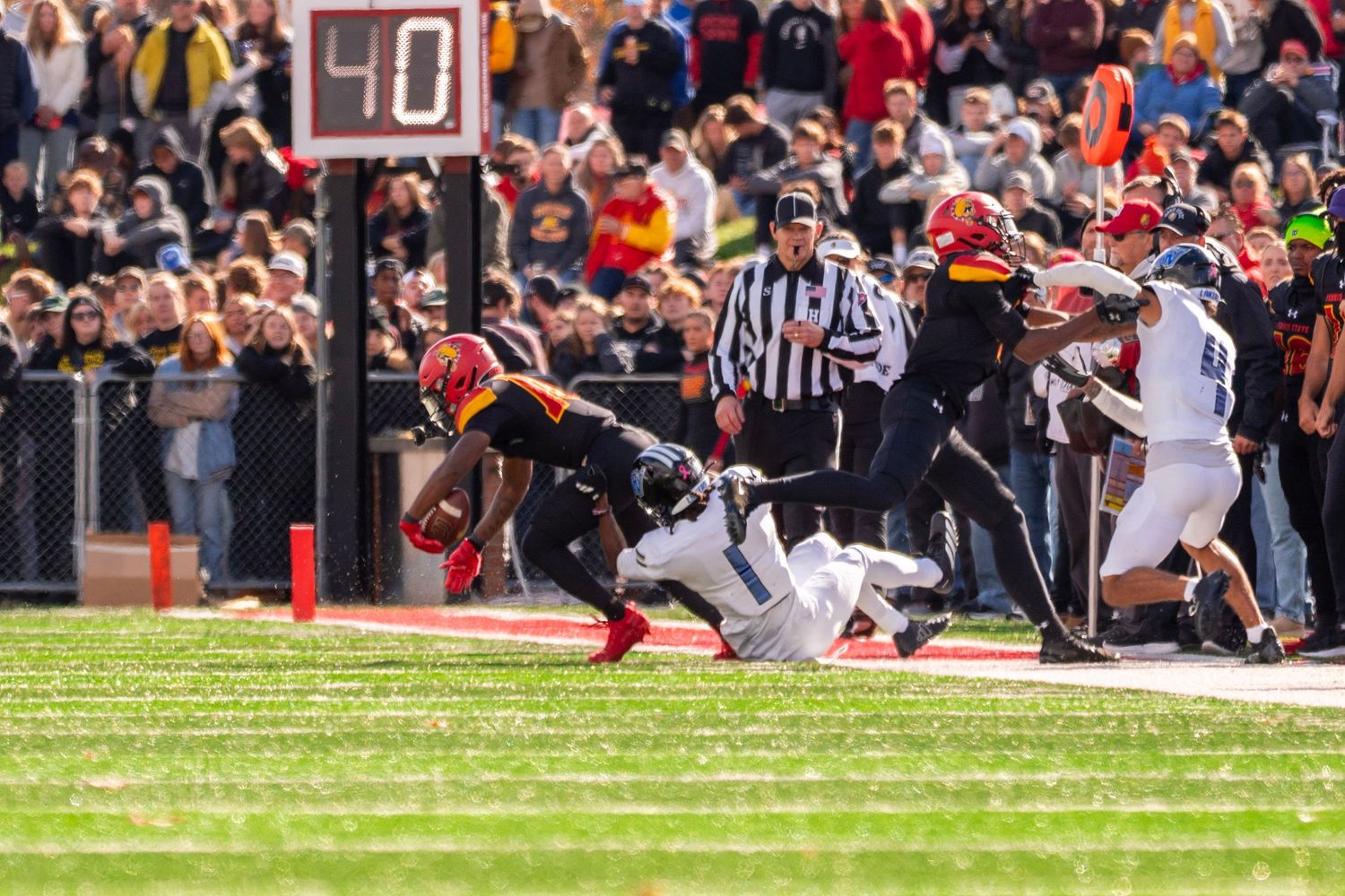 College football players collide during an intense tackle attempt near the sideline during a game.