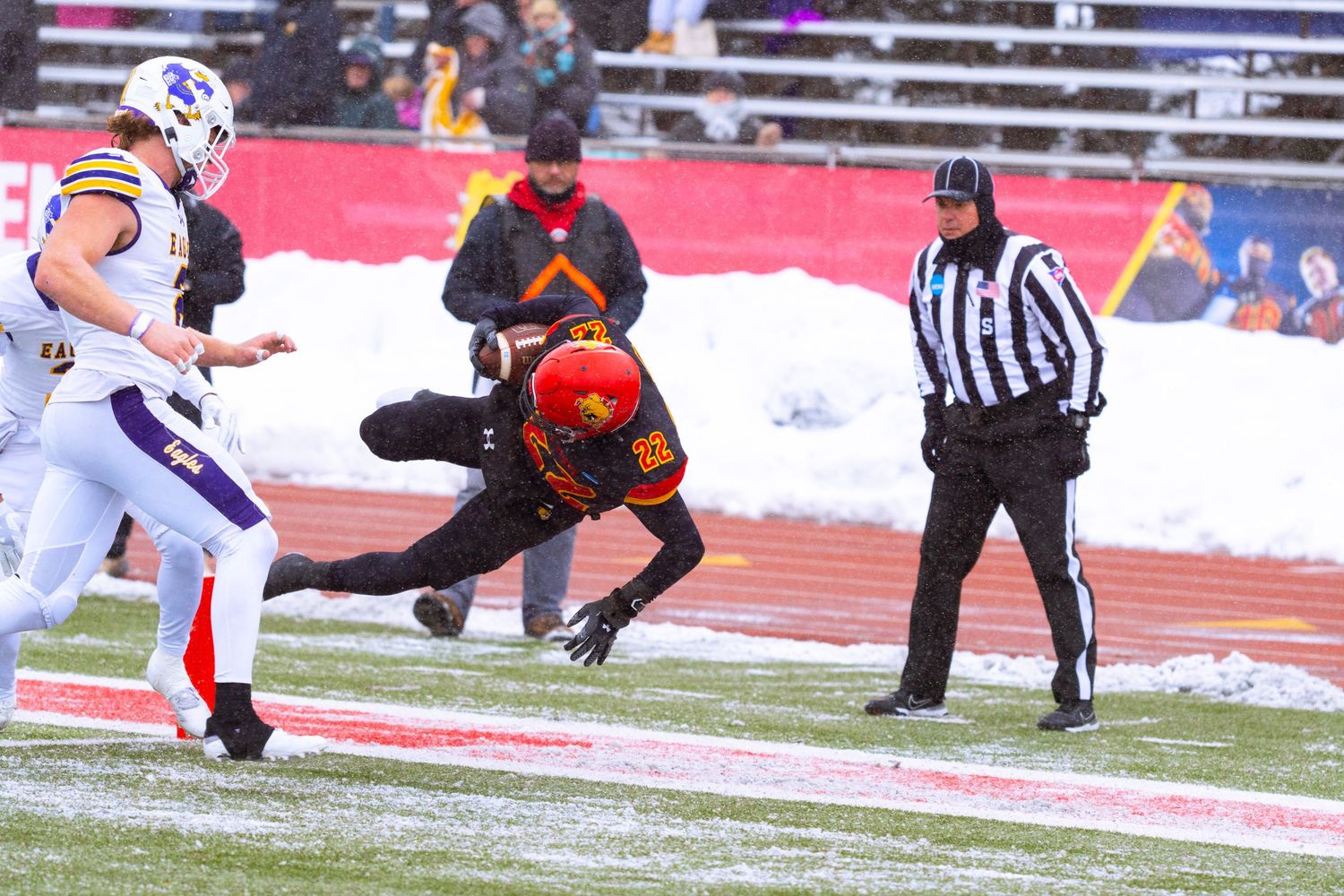 Football players battle for position on a snow-covered field during a winter match.