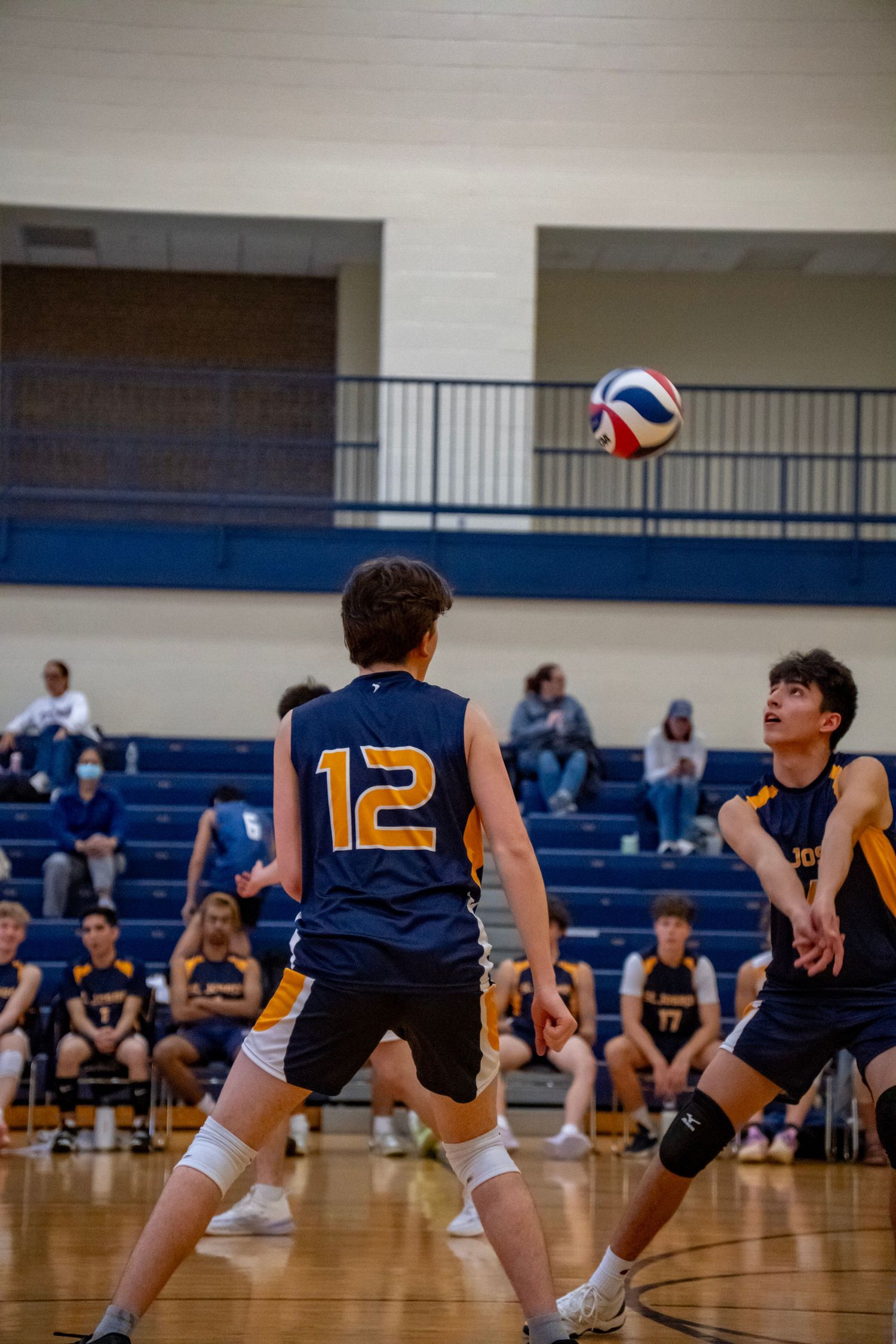Two players in navy jerseys prepare to receive a volleyball during a match.