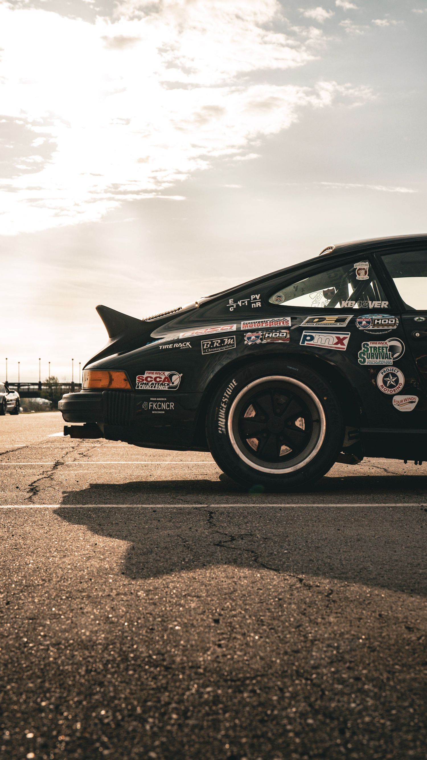 Side profile of a black Porsche 911 with racing livery and sponsor decals at sunset.