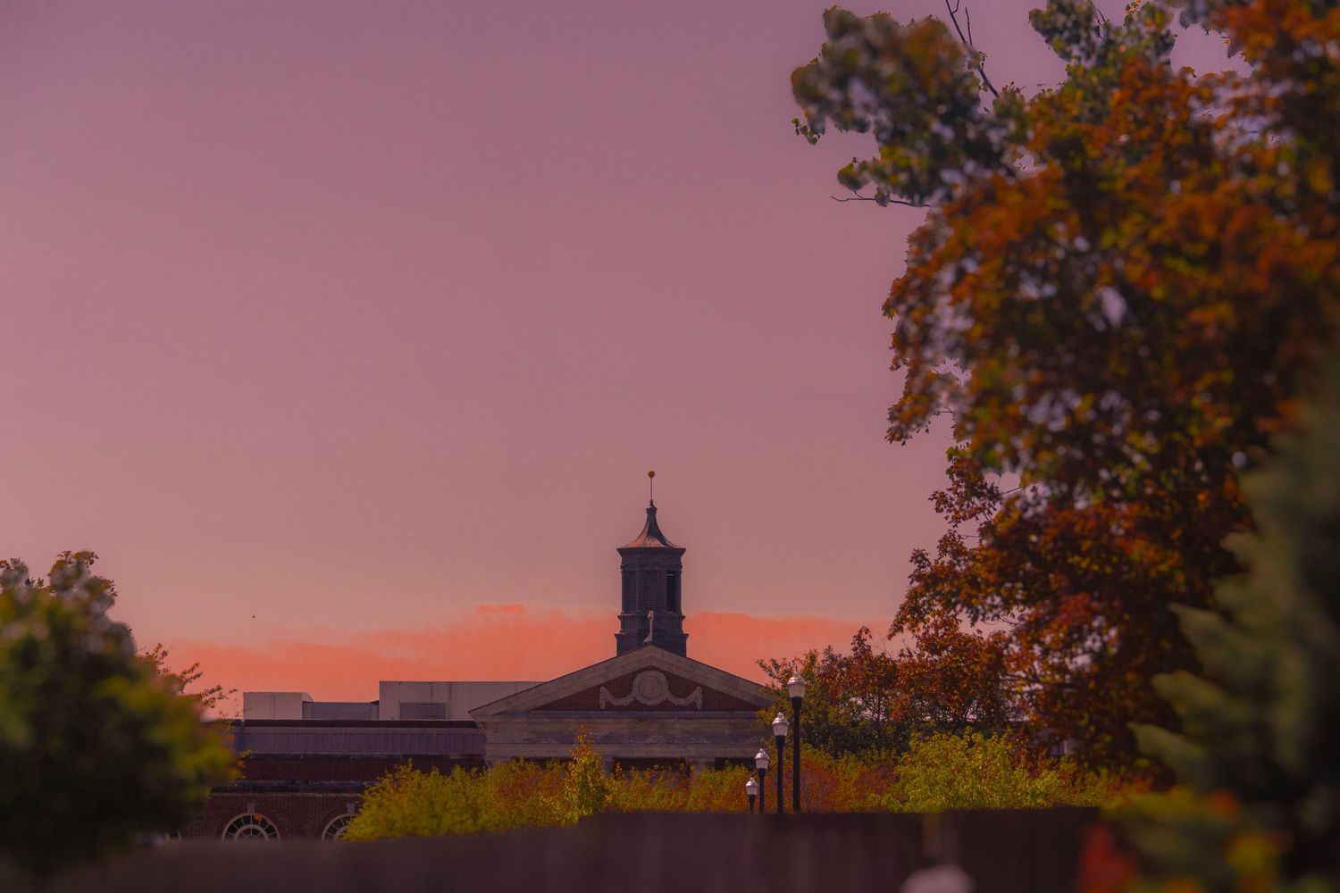 Church steeple silhouetted against pink sunset sky with fall foliage.