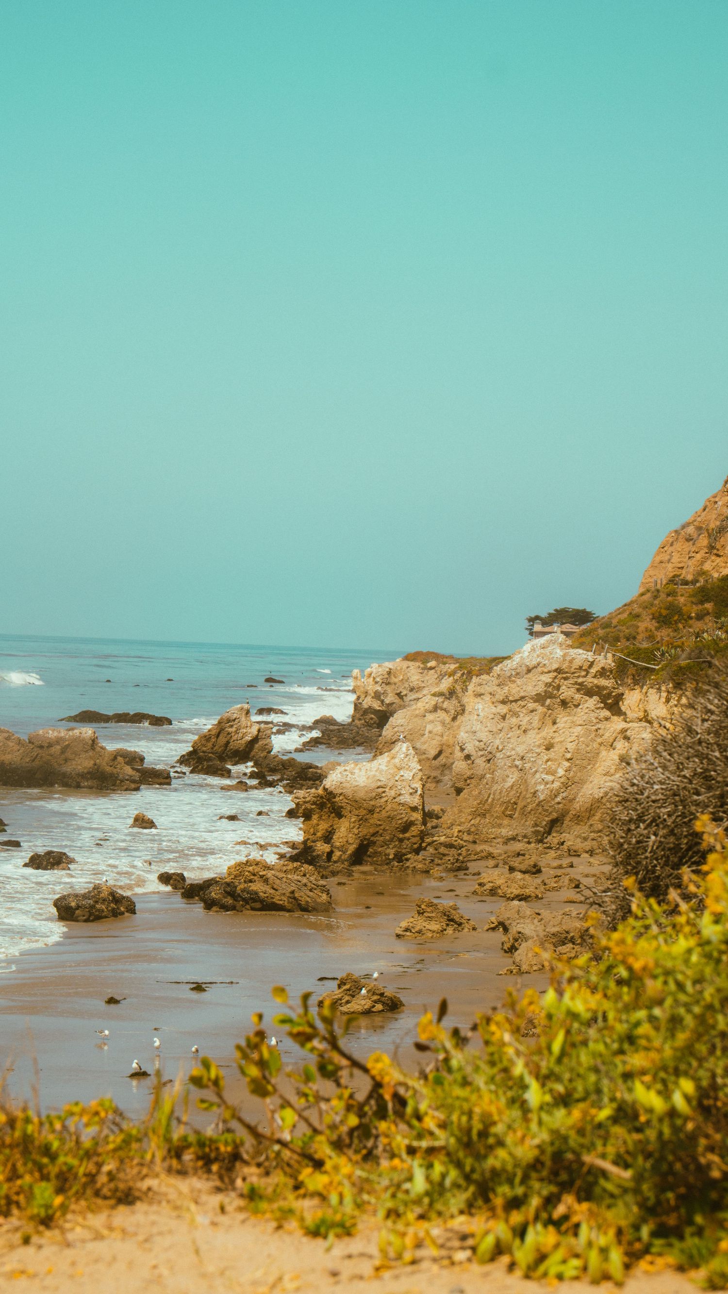 Rocky beach cove with golden cliffs and turquoise waters under clear sky.