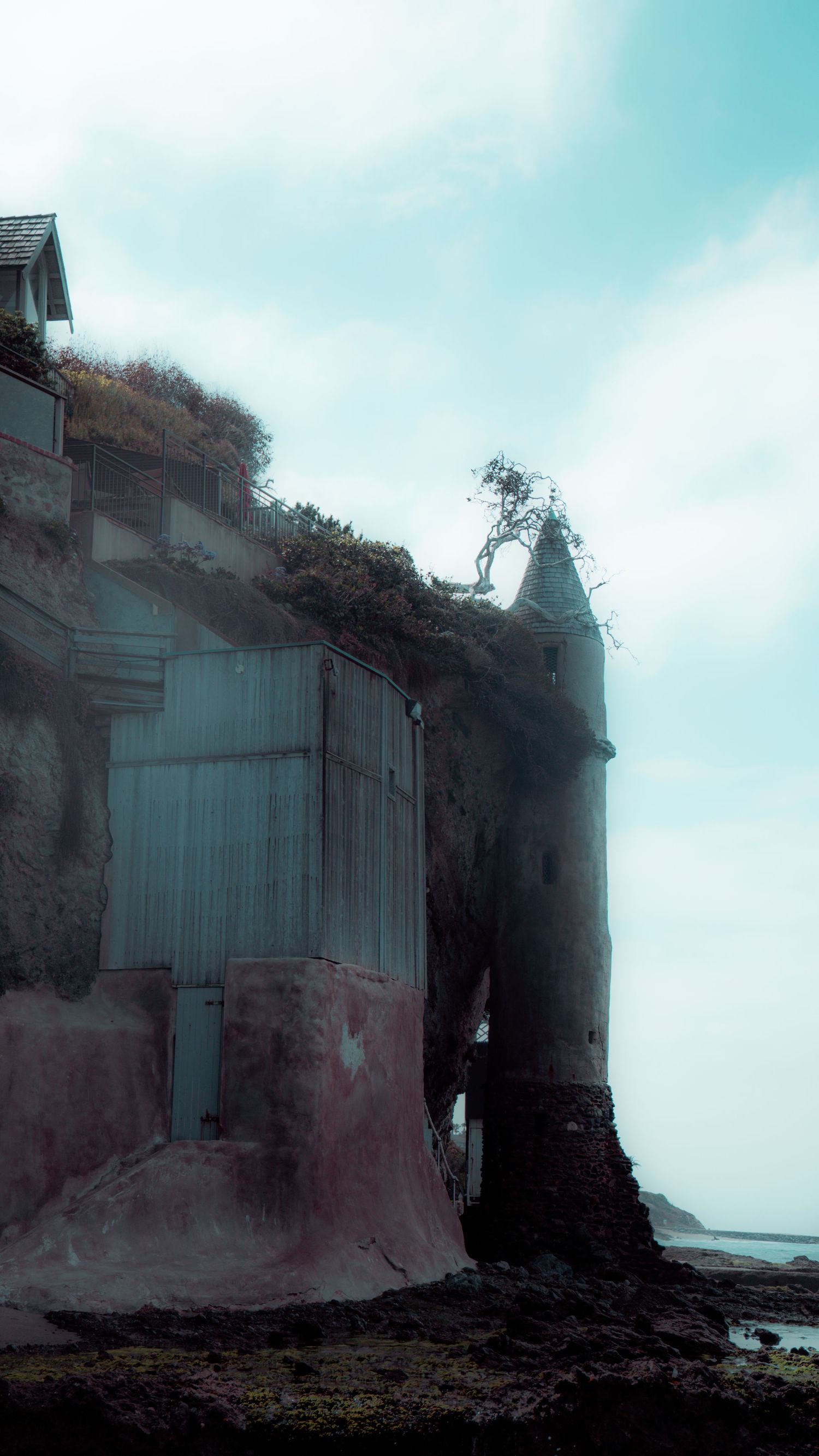 Misty coastal building with weathered walls perched on rocky shoreline.