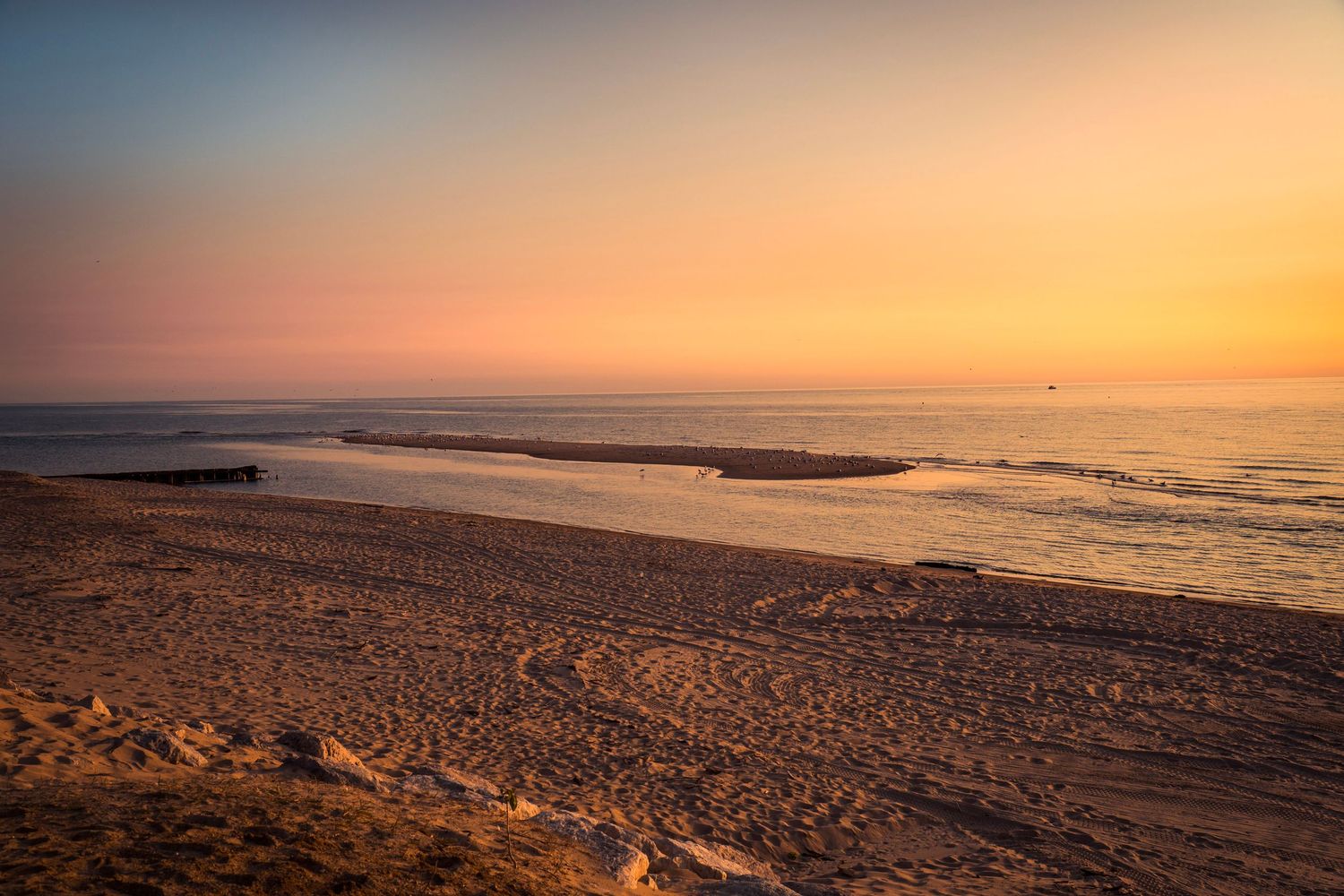 Sandy beach curves along Lake Michigan shoreline during sunset with waves rolling in.