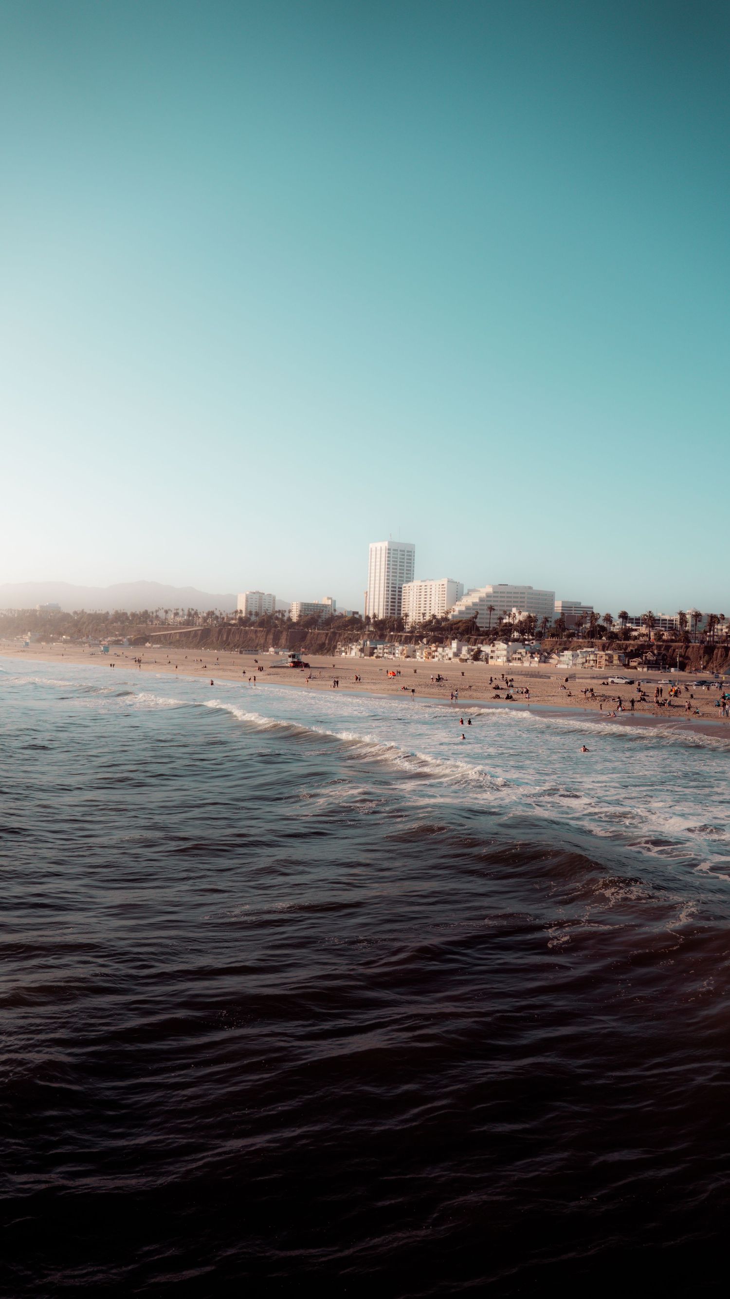 Coastal cityscape view from the ocean showing beach and high-rise buildings against clear blue sky.