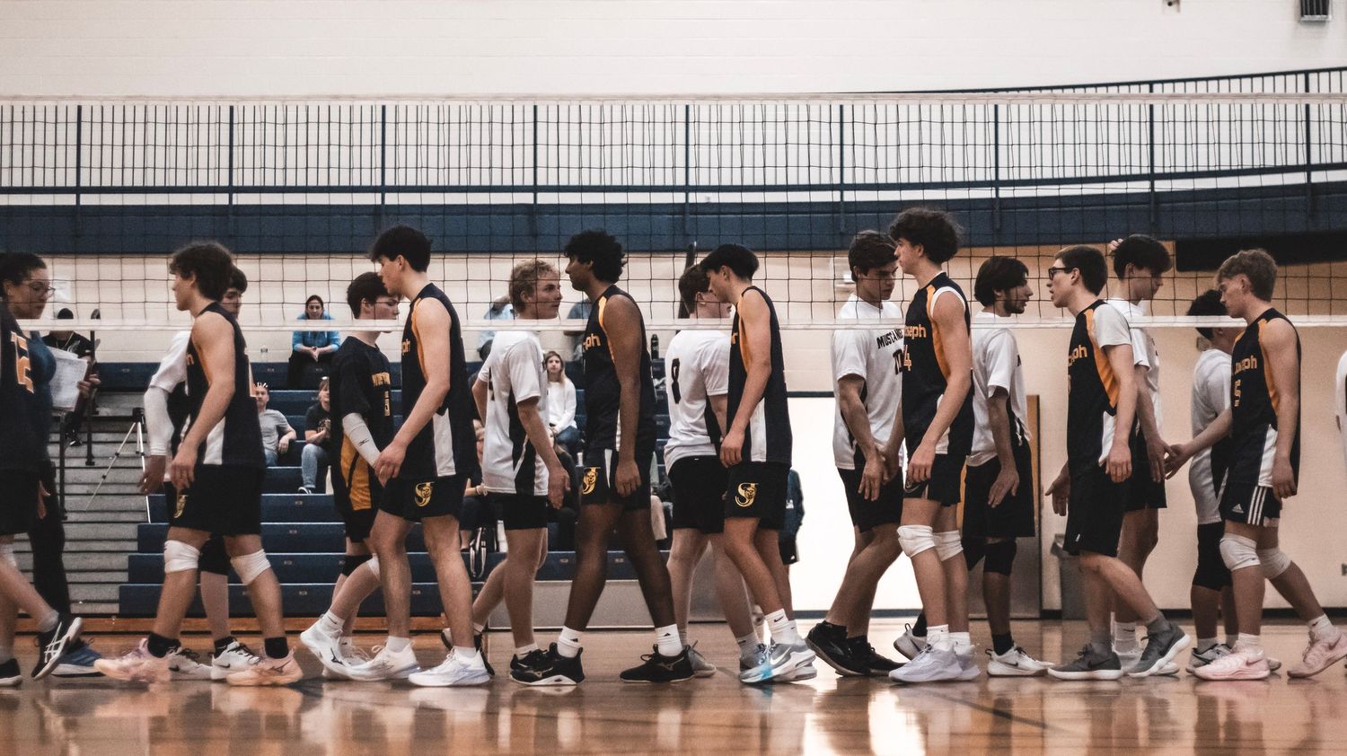 Two volleyball teams walking past each other after match in indoor gymnasium.