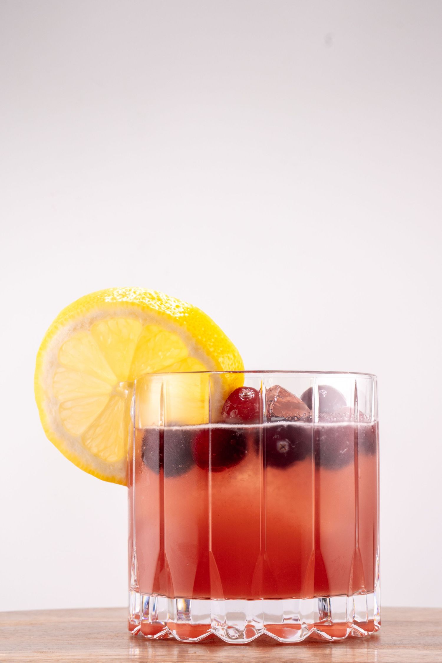 An orange-red cocktail garnished with cranberries and citrus in a crystal coupe glass.