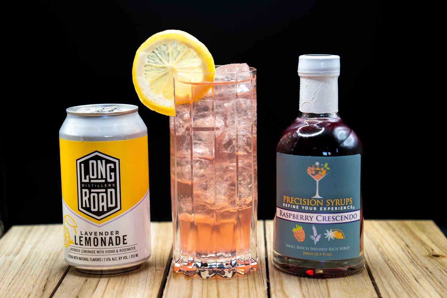 Artisanal drink setup with canned lemonade, garnished cocktail and craft spirits on wooden backdrop.