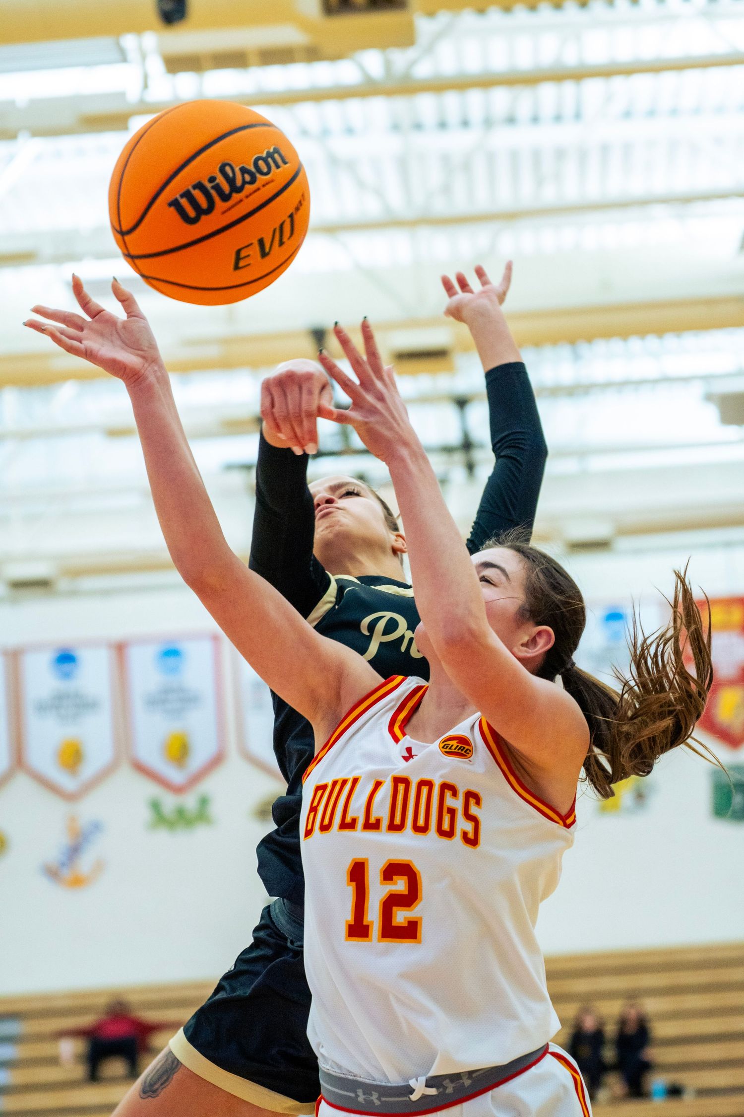 Basketball players jump for a rebound during an intense game between teams in orange and black uniforms.