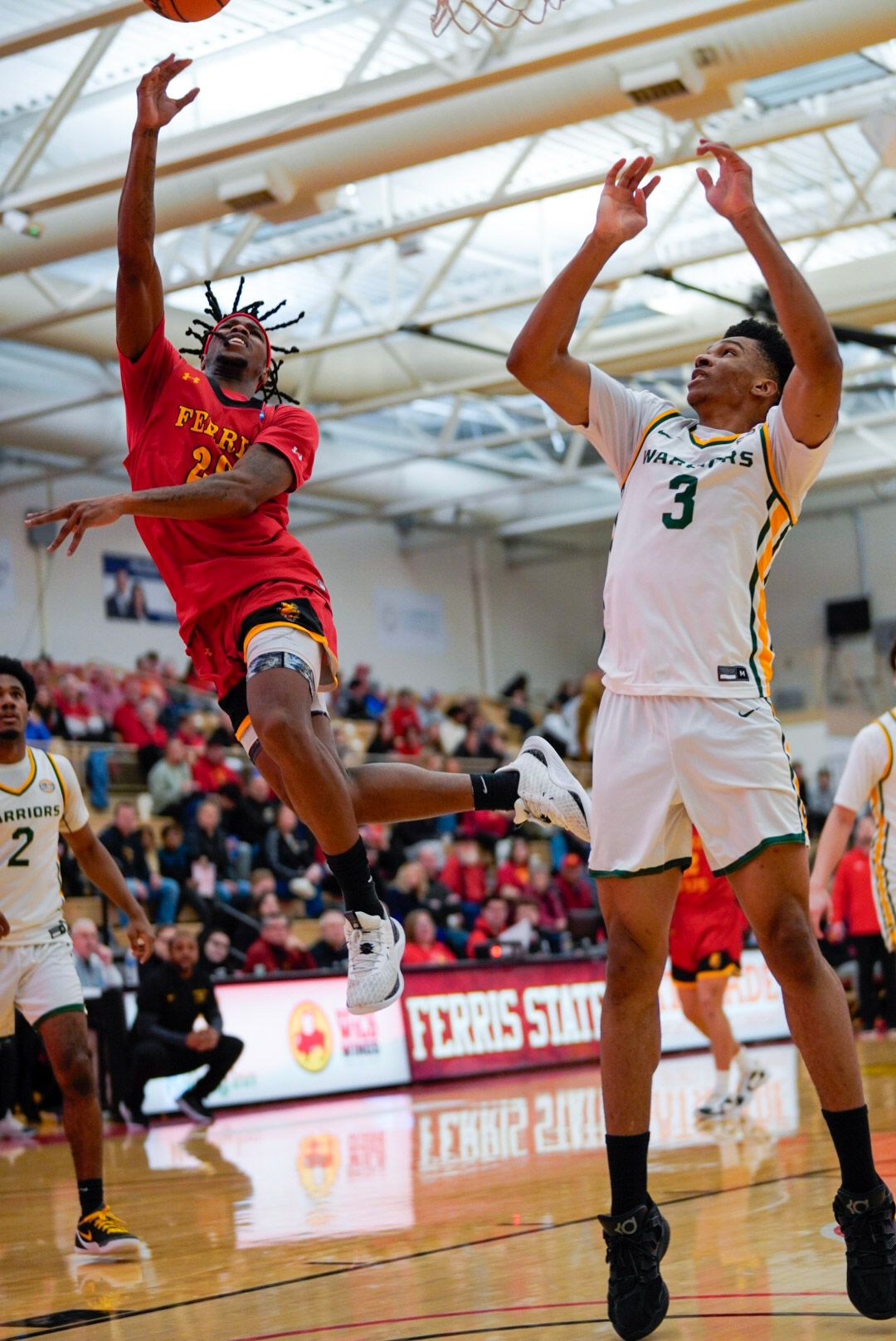 Basketball players leap high to compete for a rebound during an intense indoor game at a gymnasium.
