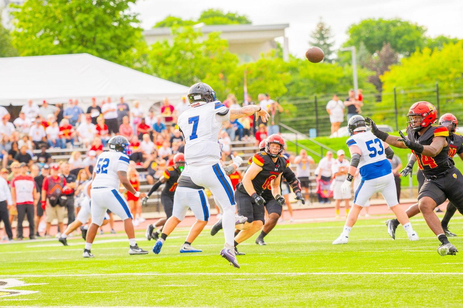 Football players in white and black uniforms battle on a green field as the ball soars through the air while fans watch from the stands.