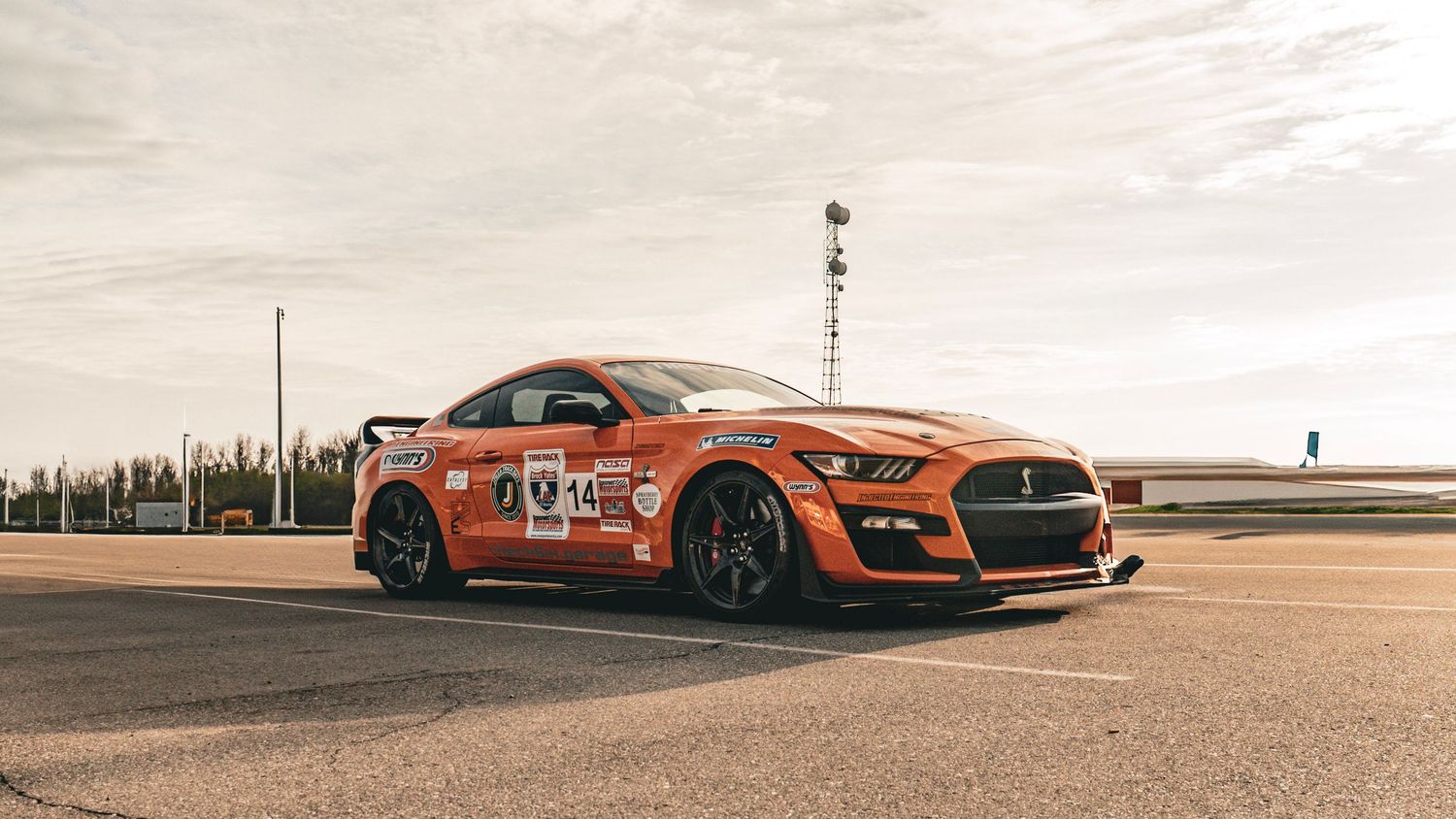 Side profile of orange Mustang GT500 race car with aerodynamic modifications on track.