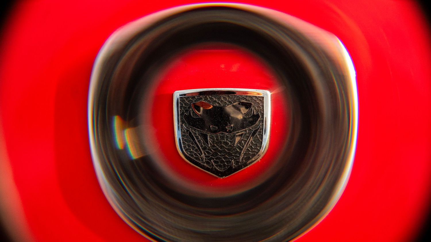 Artistic shot of Dodge viper emblem through circular lens with red background.
