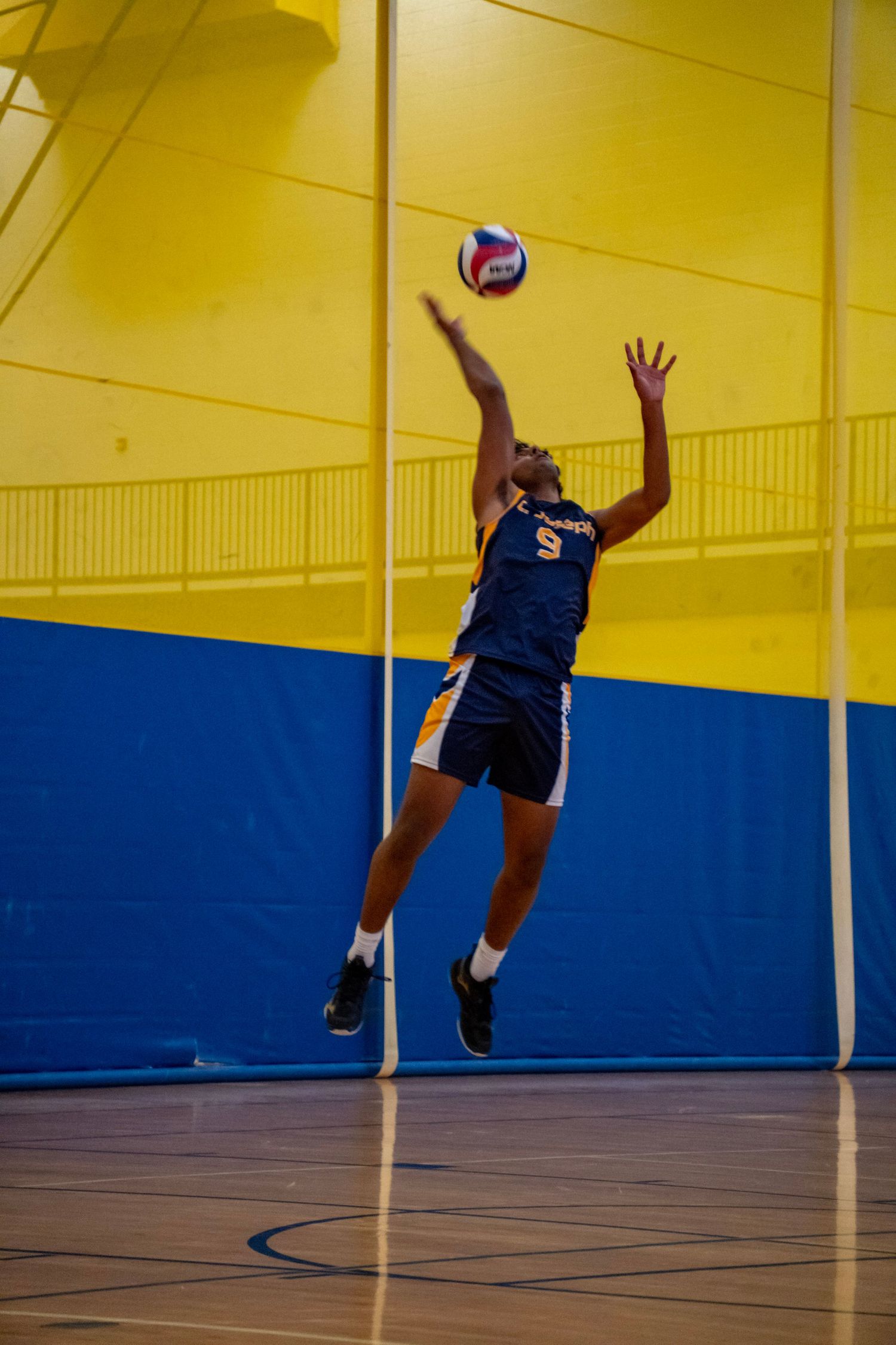 Volleyball player in navy uniform jumps to hit the ball during a match.
