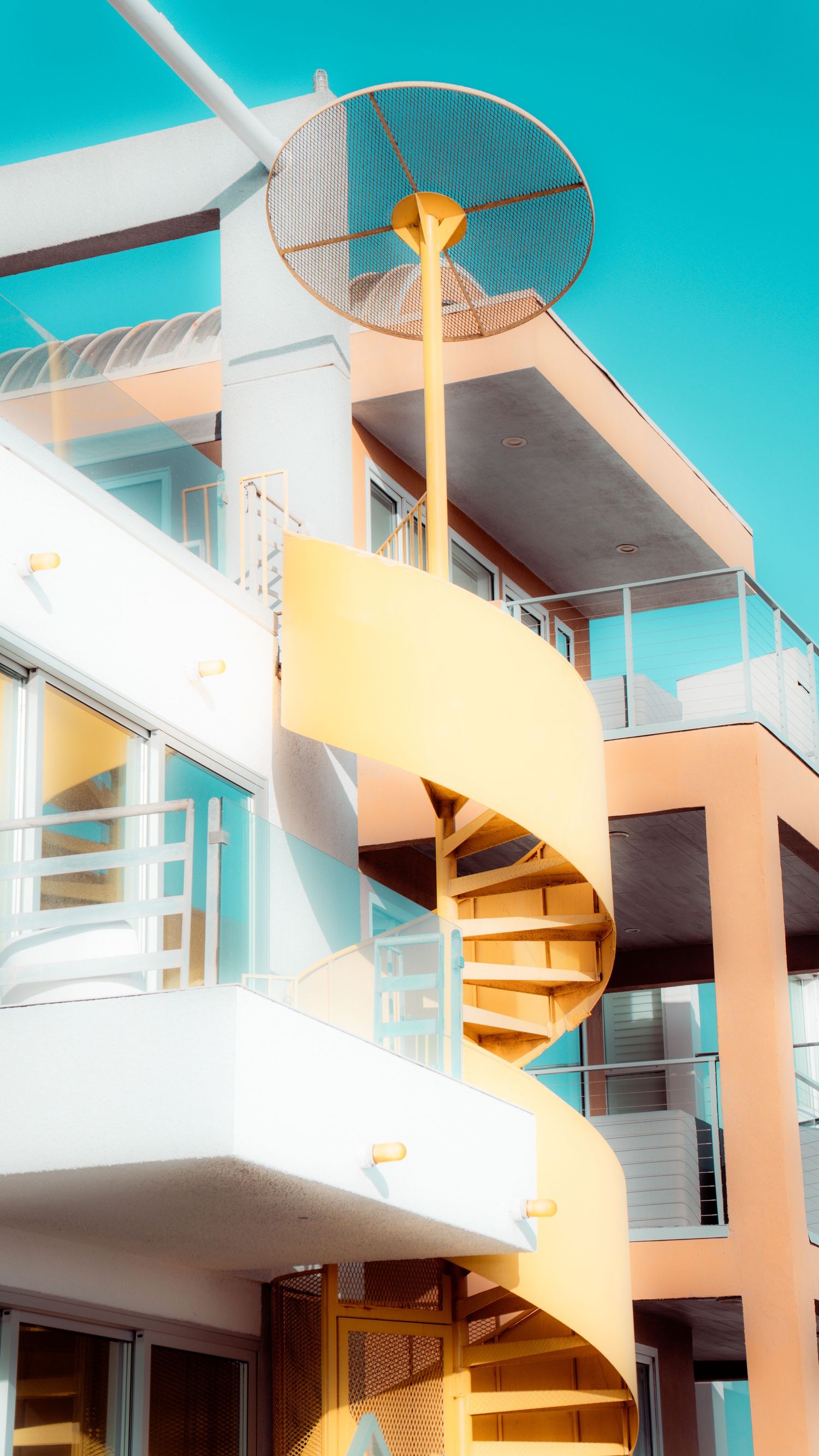Modern apartment building with white exterior and spiral staircase against bright blue sky.