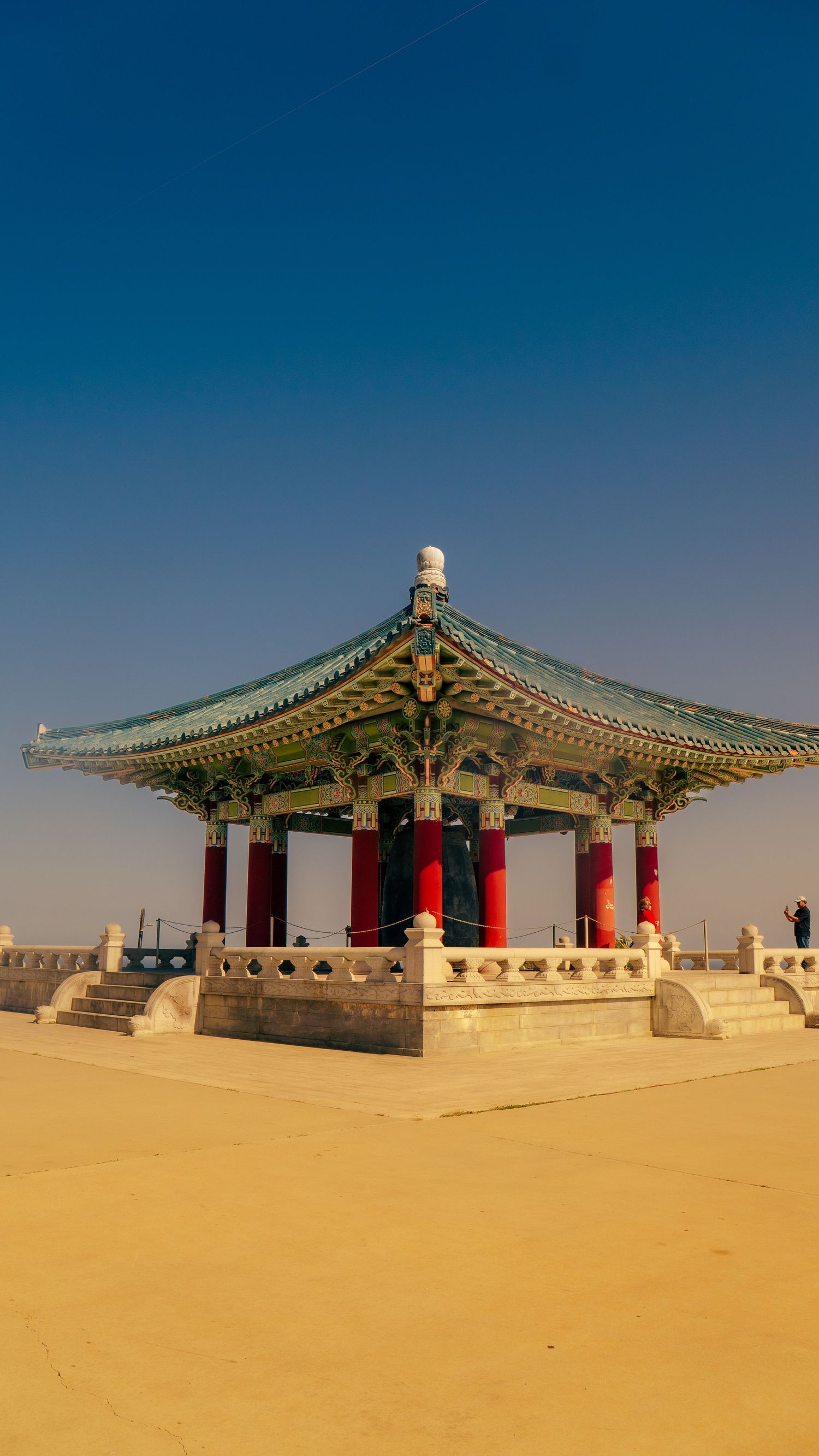 Korean bell pavilion with ornate green roof and red pillars in desert setting.