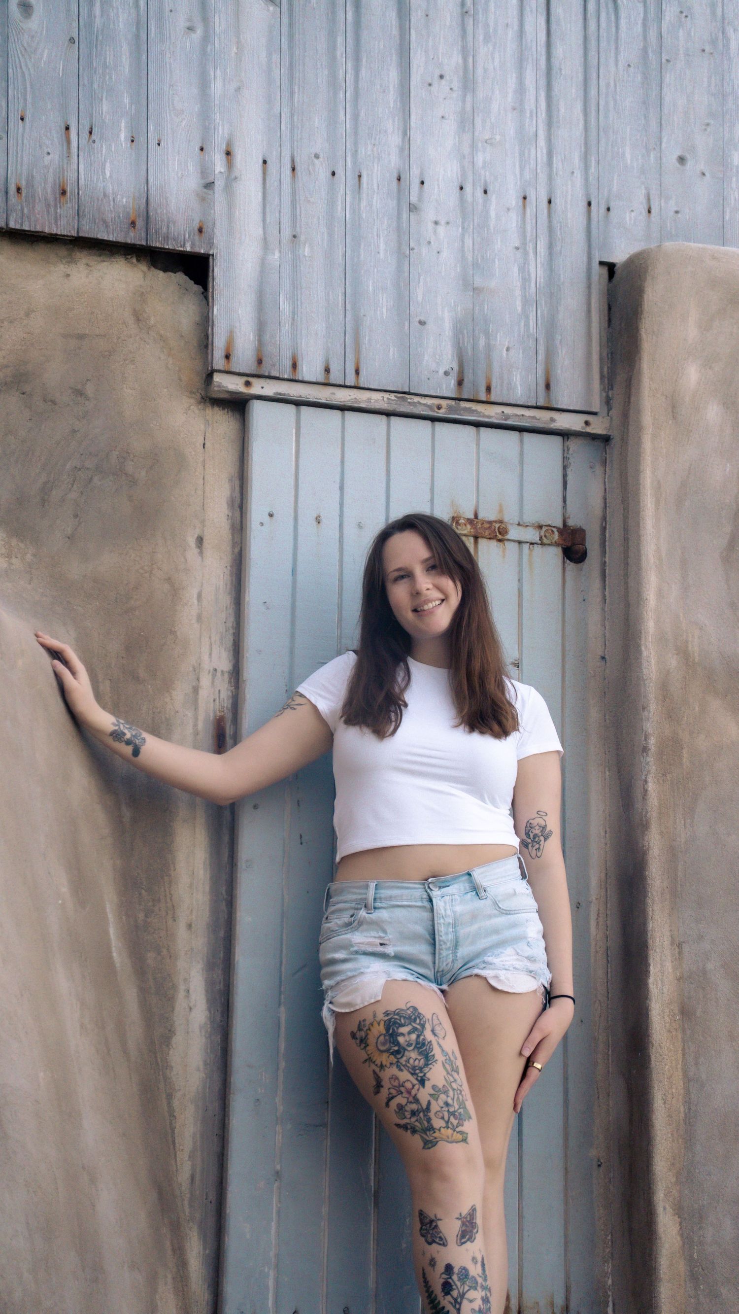 Figure posing next to blue wooden door wearing crop top and distressed denim shorts.