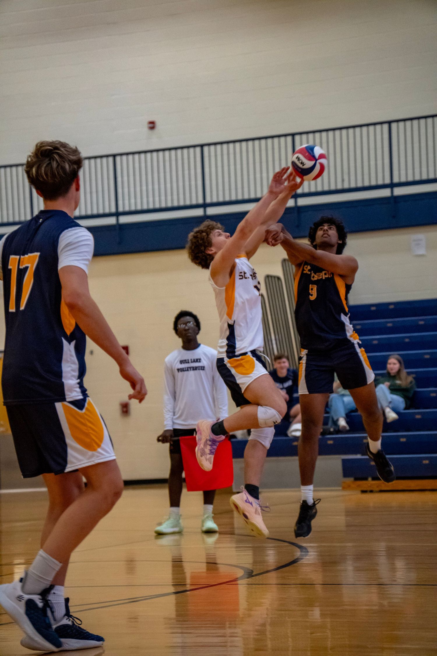 Players jumping to block a volleyball spike during an indoor match.