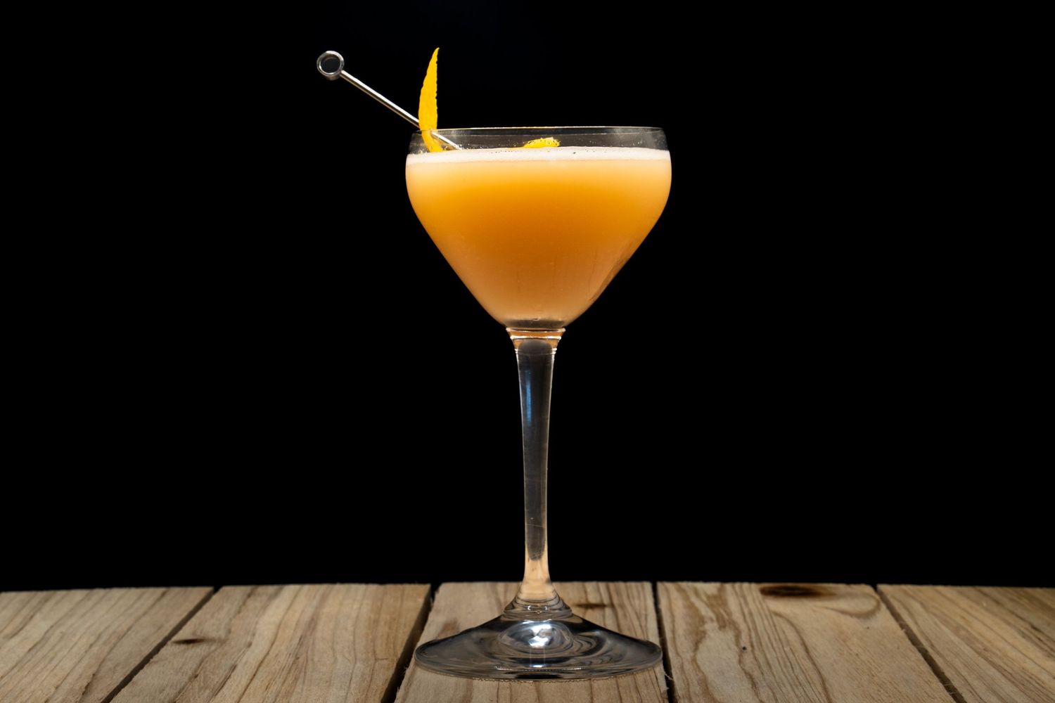 Elegant orange cocktail served in coupe glass with citrus garnish against black background.