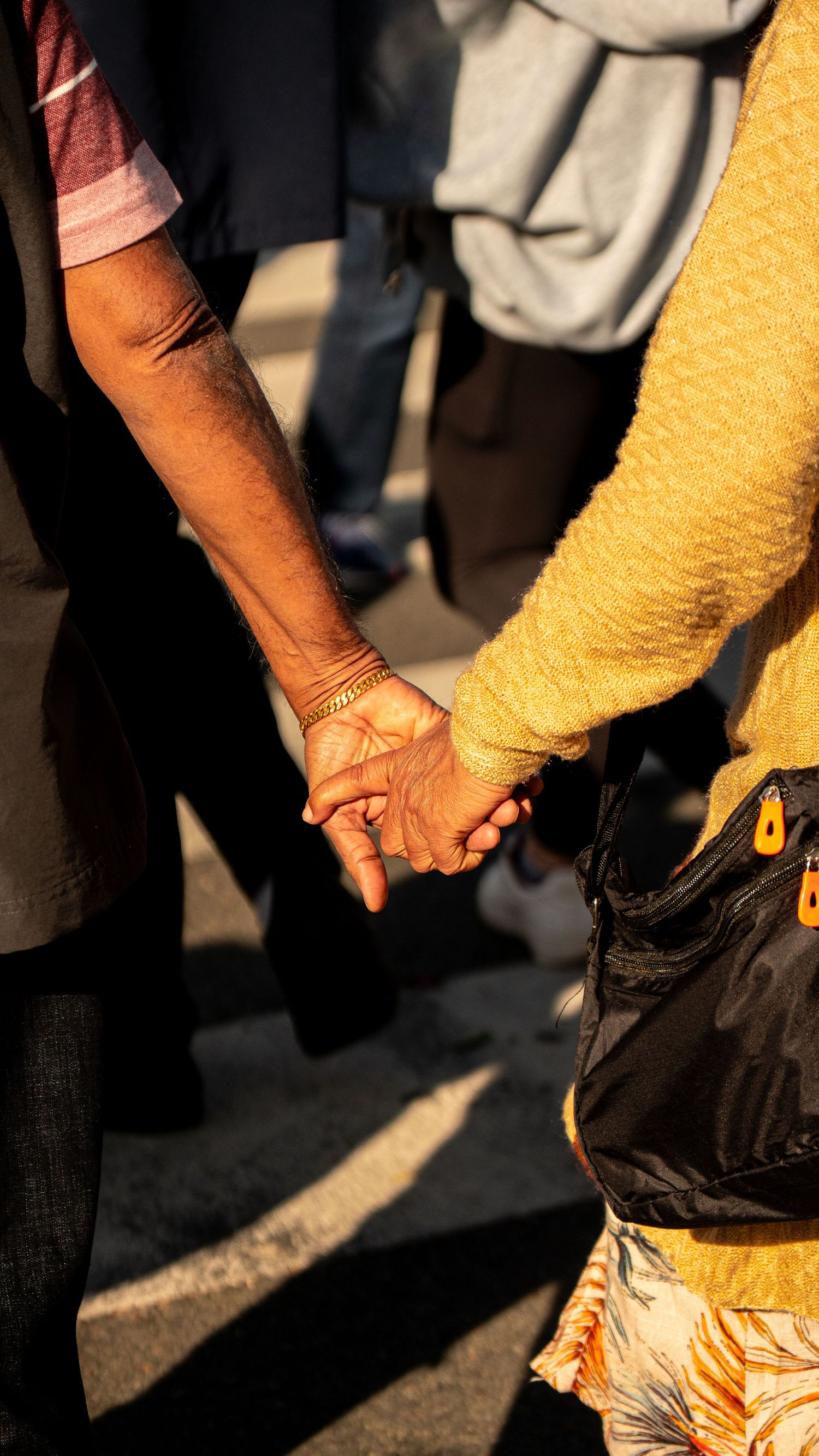 Close-up of two people holding hands in warm sunlight with yellow fabric visible.