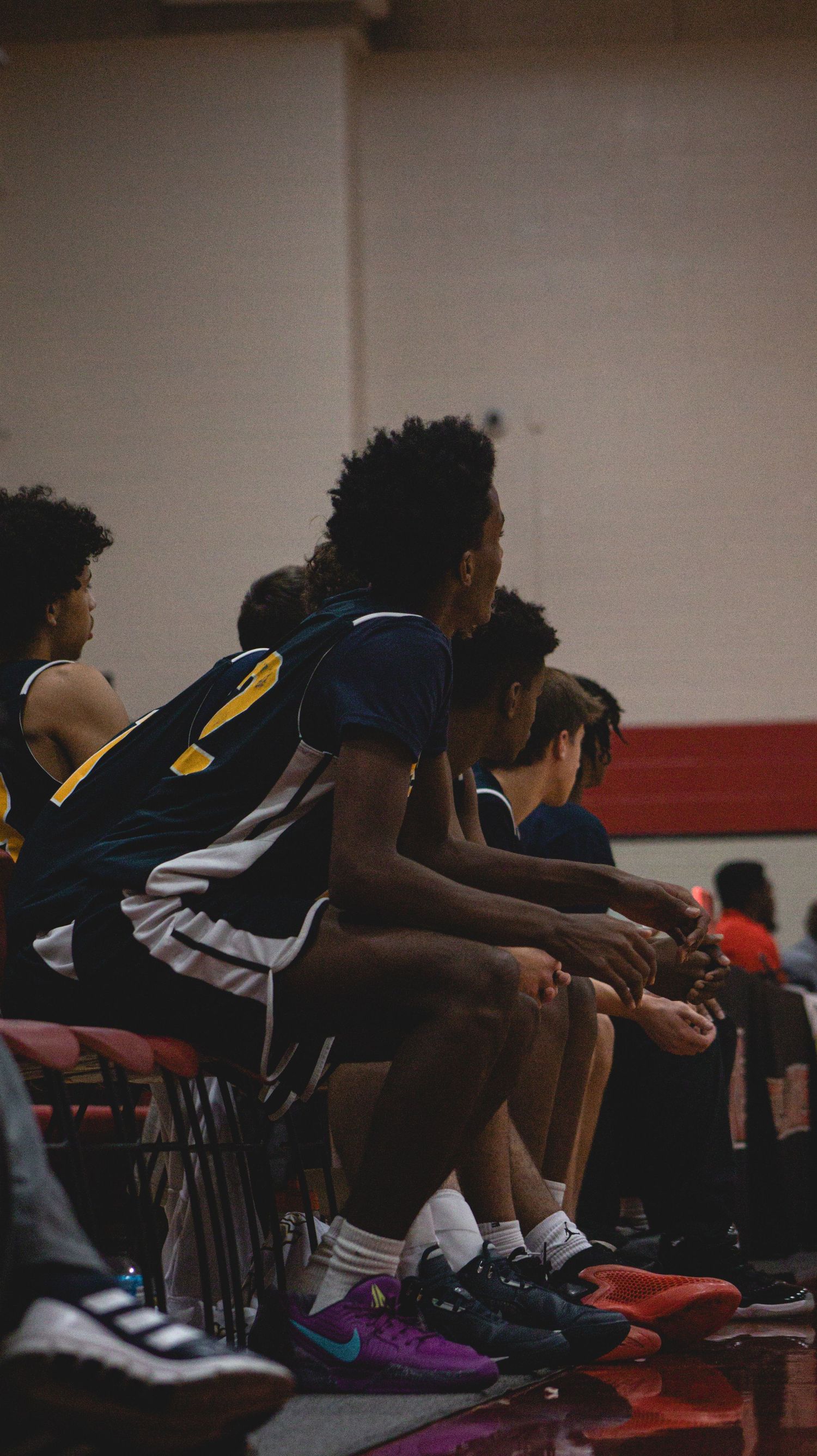 Players resting on chairs during a basketball game break in dark lighting.