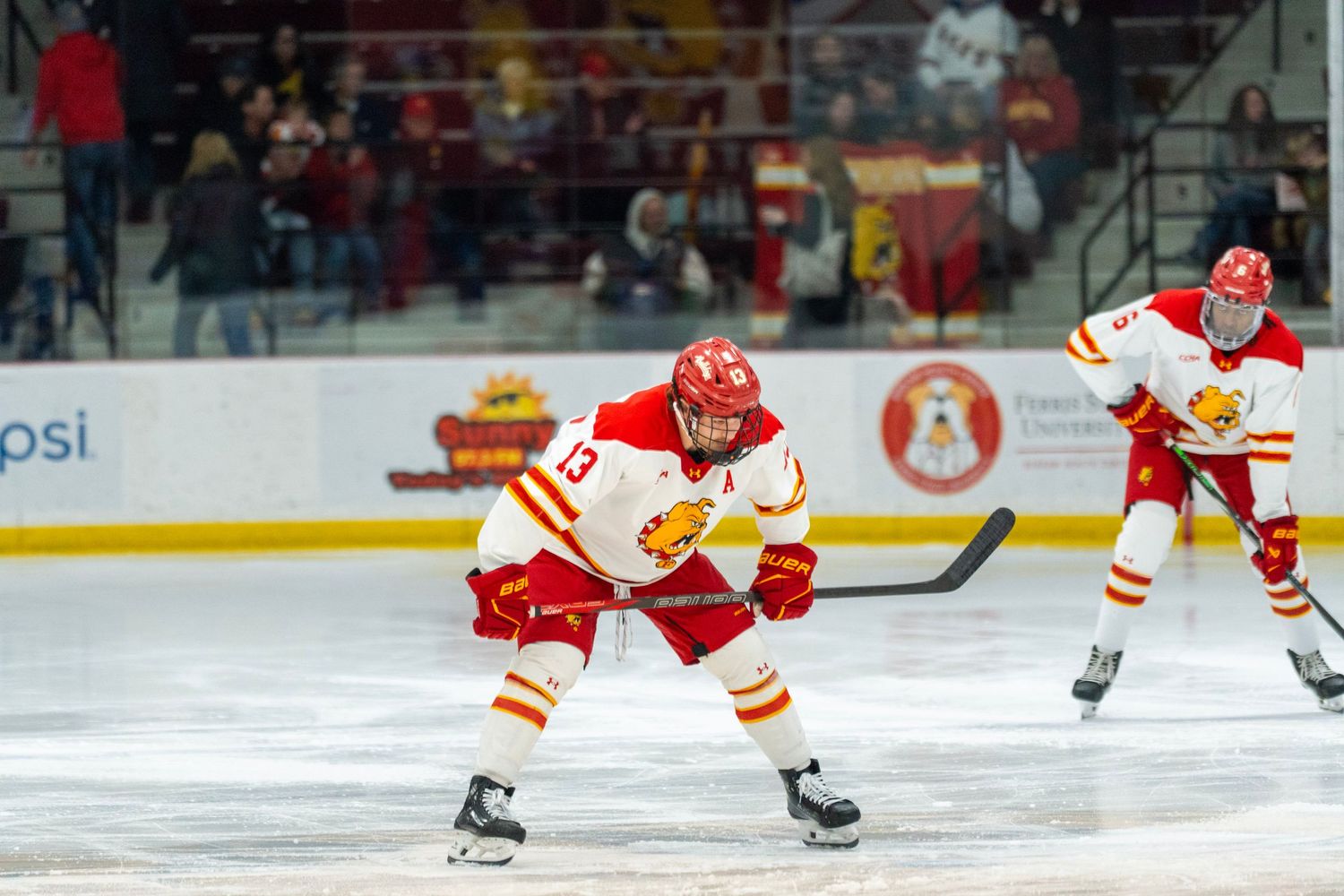 Hockey player in red and white uniform skates with puck during competitive match on ice rink.