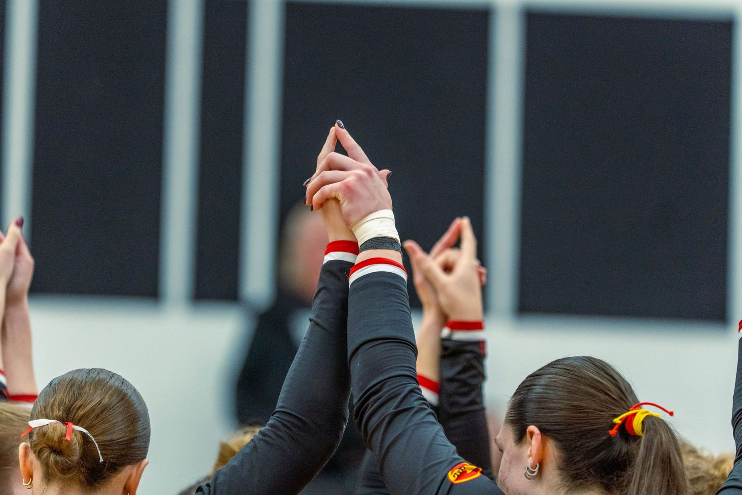 Volleyball teammates huddle with hands raised together in a pre-game unity ritual.
