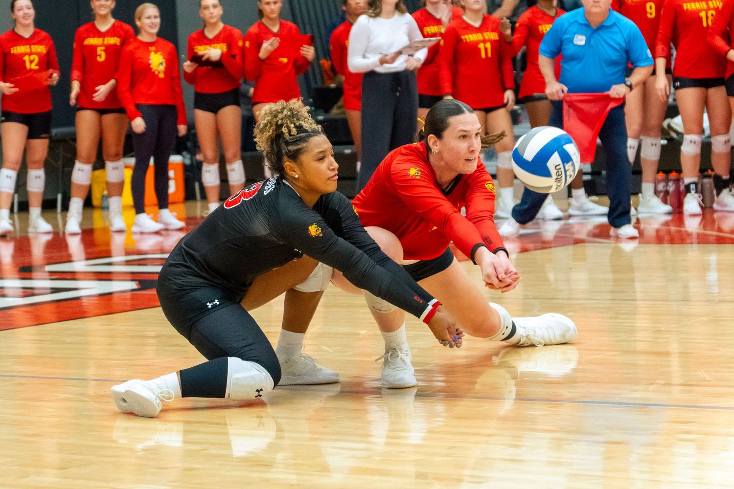 Volleyball players stretch on a gymnasium court before a match while wearing red uniforms.