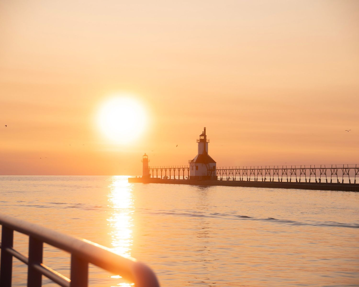 St. Joseph lighthouse casts reflection on Lake Michigan waters during brilliant orange sunset.