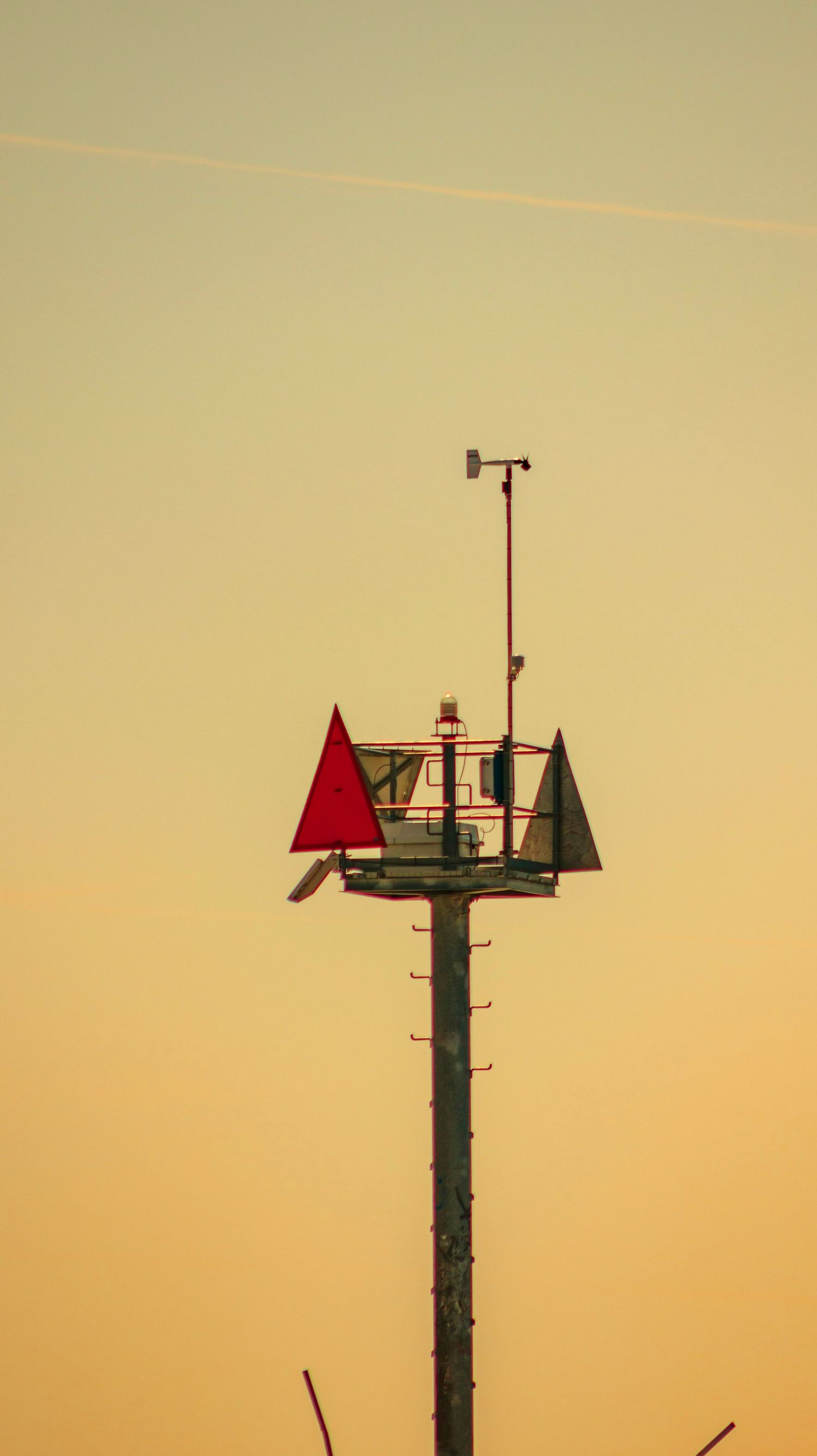 Navigation marker tower with red triangle against golden sunset sky.