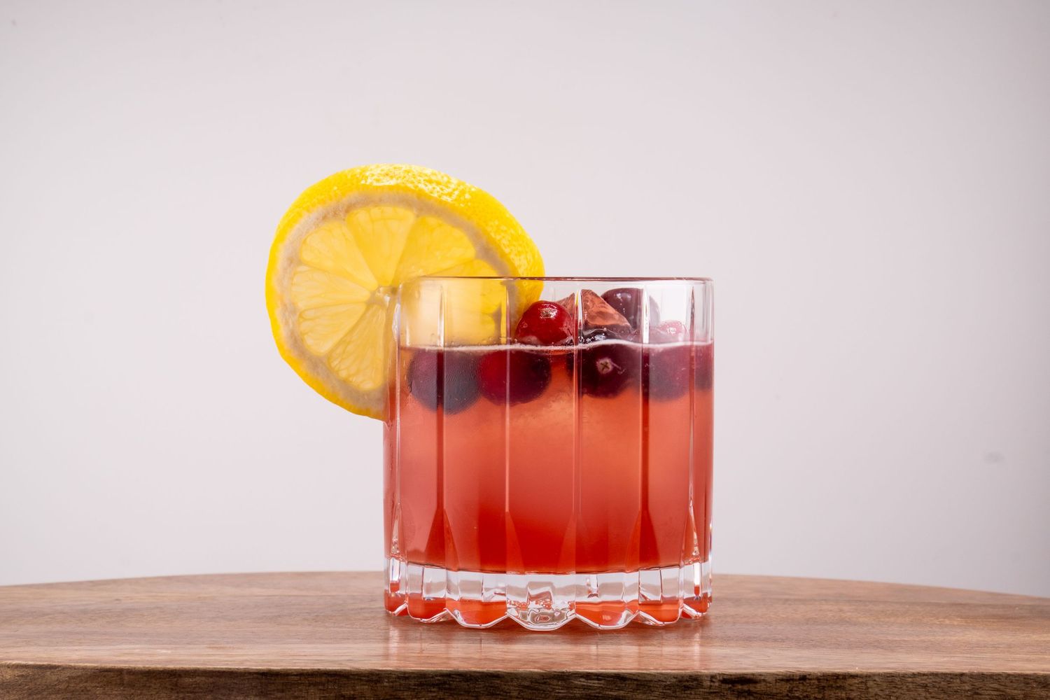 Red craft cocktail garnished with orange slice in cut crystal glass.