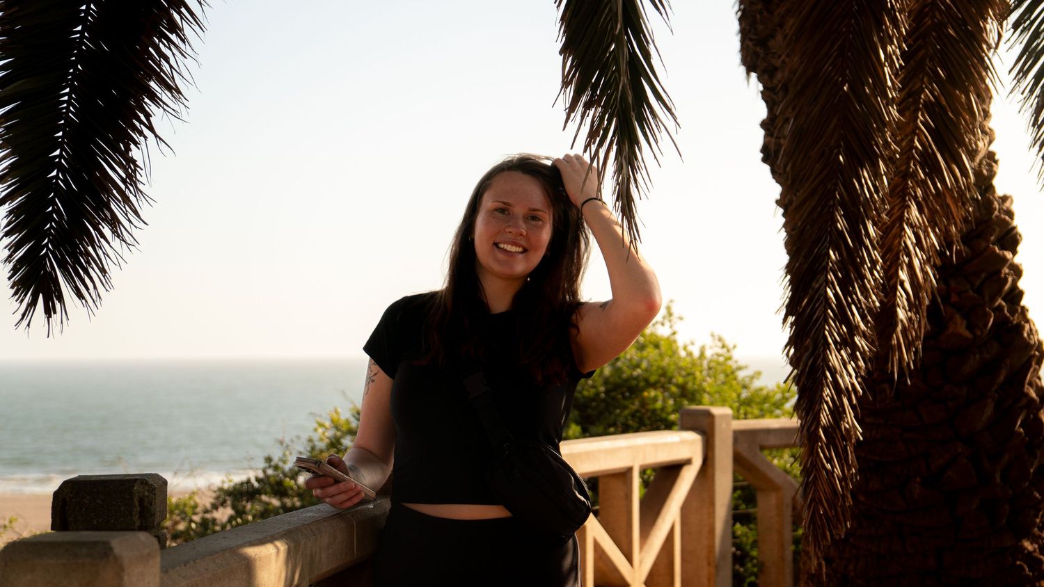 Casual pose beneath palm trees with ocean vista in background during golden hour.