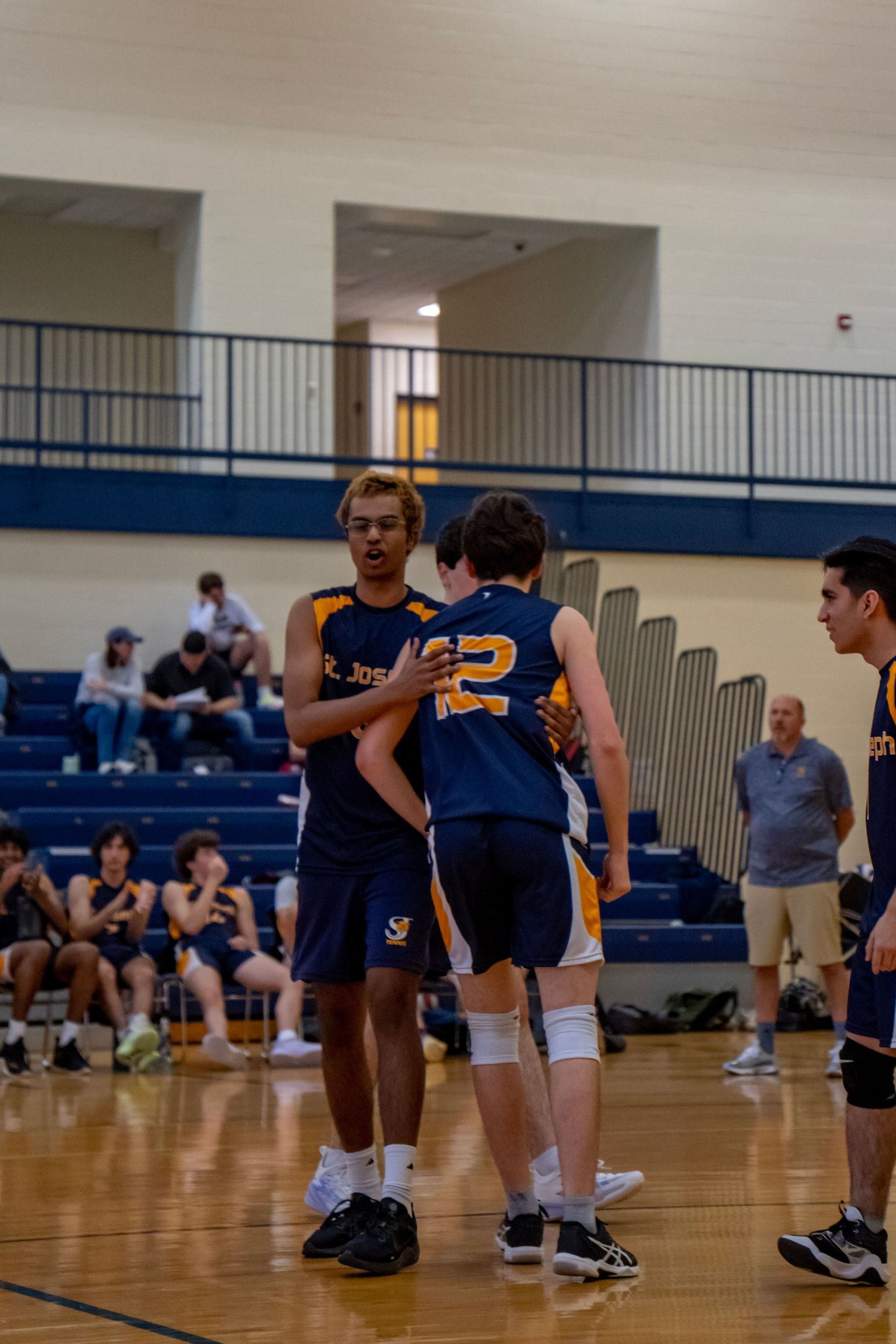 Volleyball players in navy and gold uniforms position themselves on the court during a game.