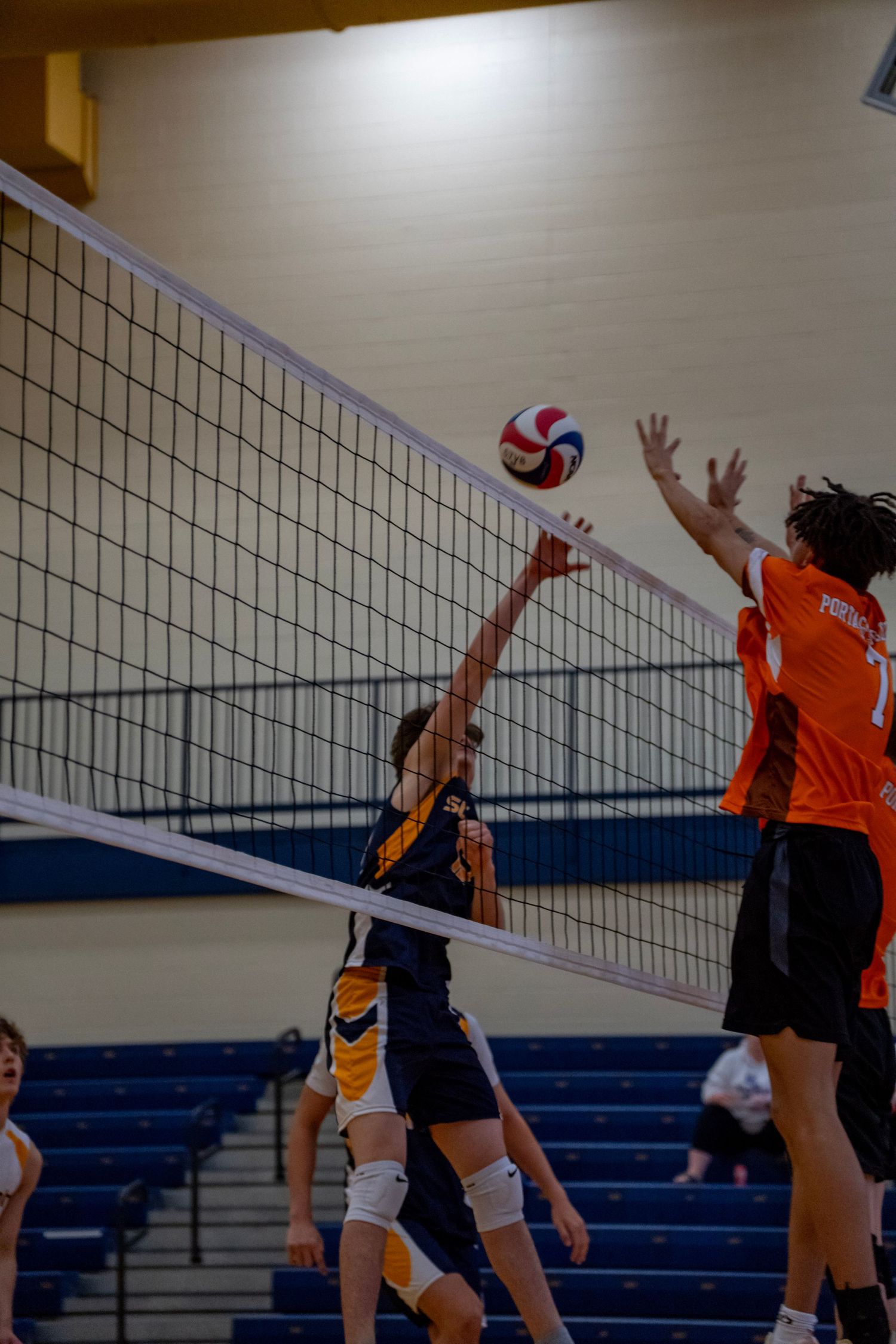 Players jump at the net during a competitive volleyball point at a school gymnasium.