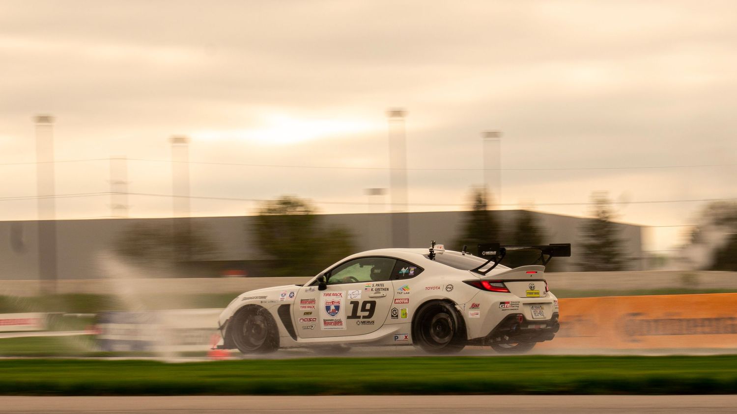 Race cars speeding past on a race track with motion blur effect at sunset.